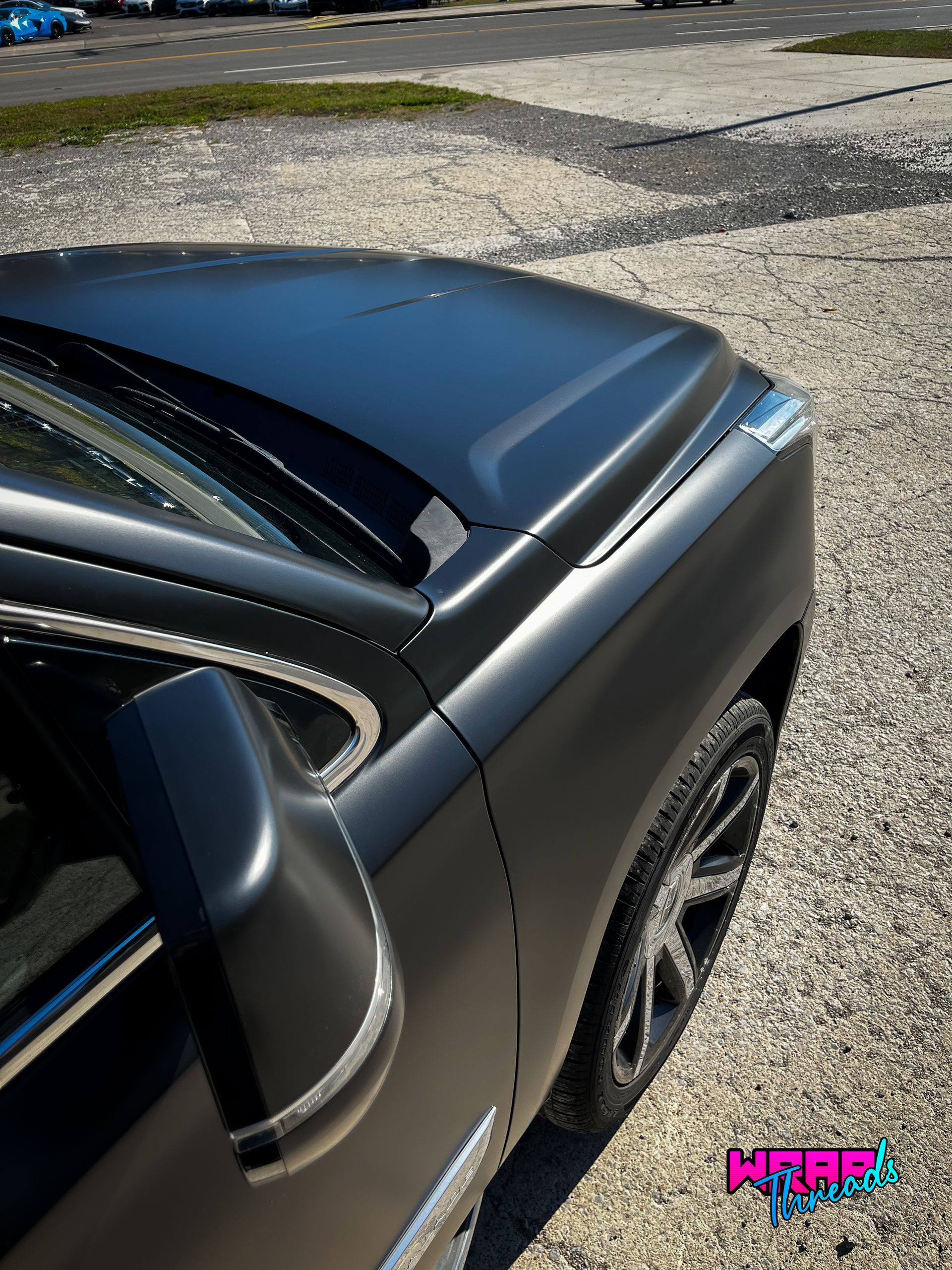 A matte charcoal-wrapped vehicle hood and side panel viewed from an elevated angle on a gravel lot.