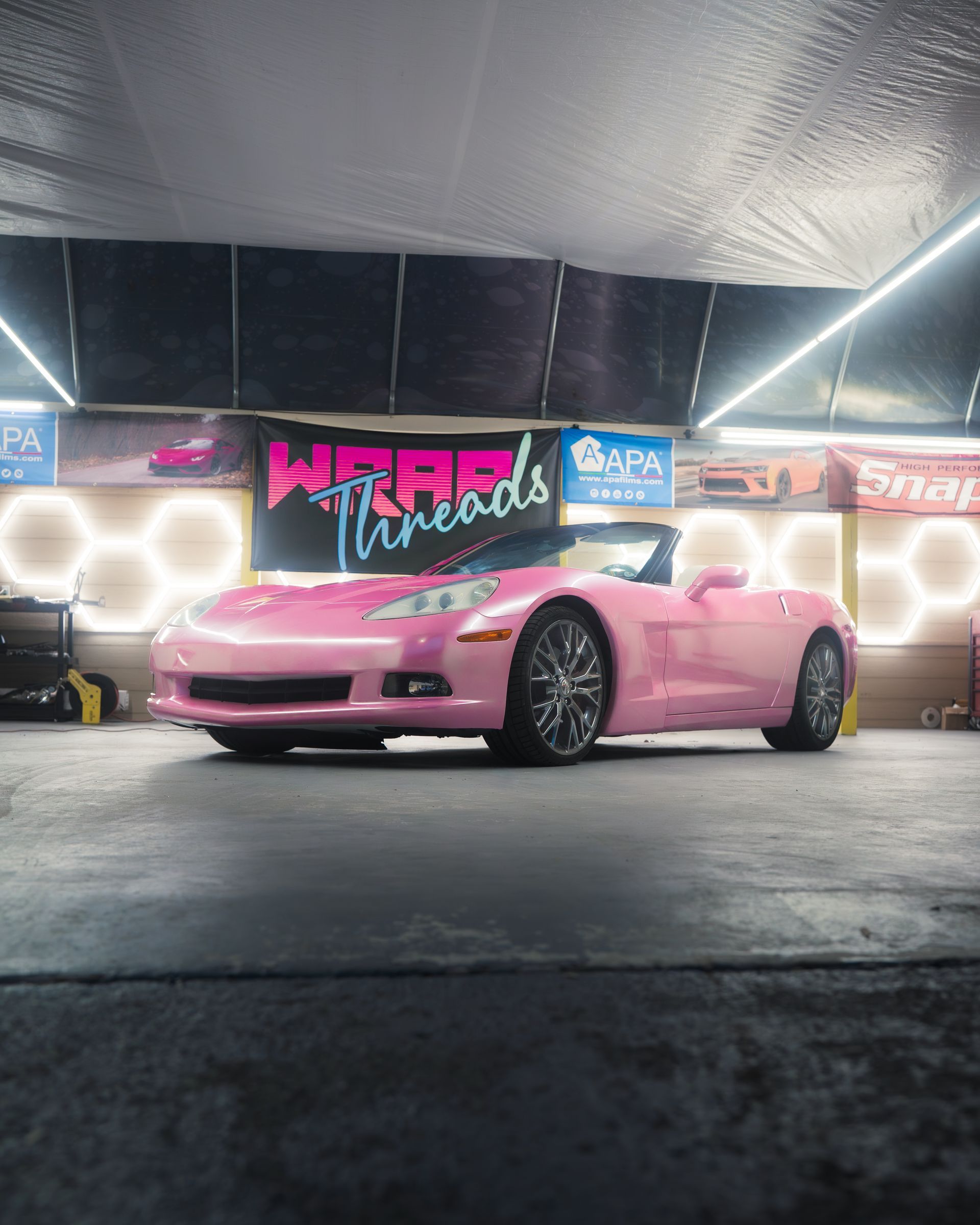 A pink convertible Chevrolet Corvette parked in a garage with 