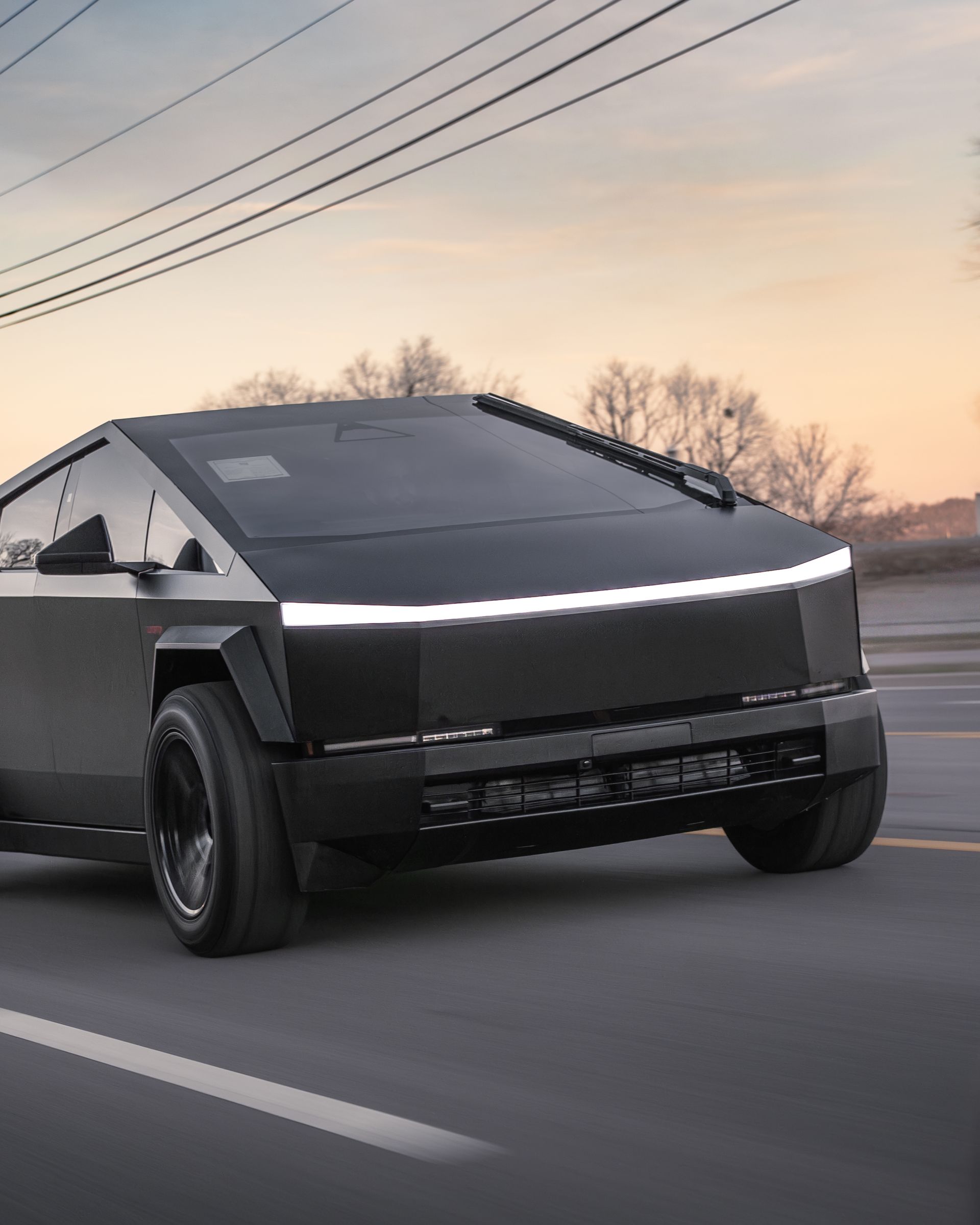 A matte black Tesla Cybertruck driving on an asphalt road during a sunset.