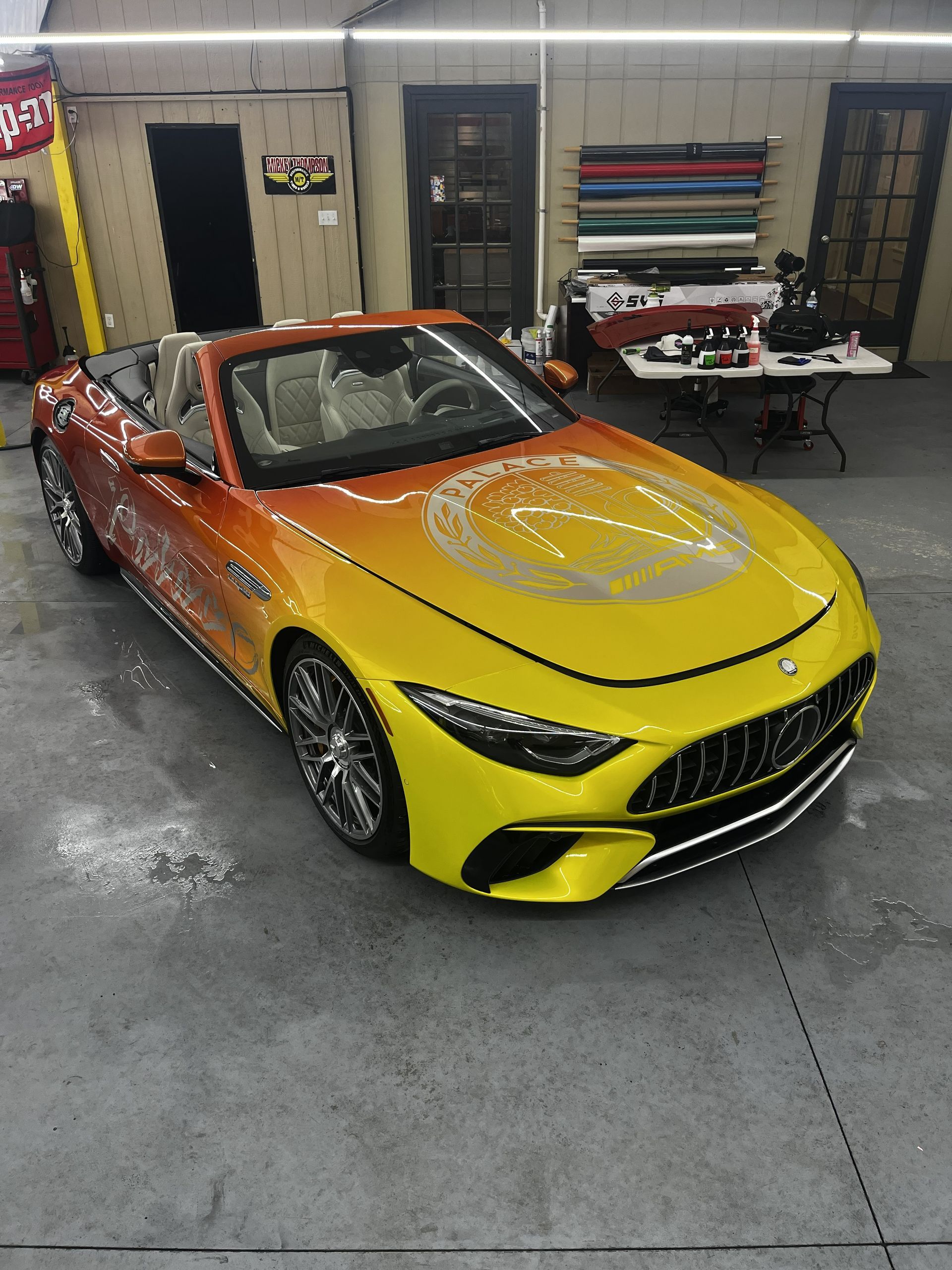 A yellow-to-orange gradient convertible Mercedes-Benz SL parked inside a workshop with a custom hood decal.