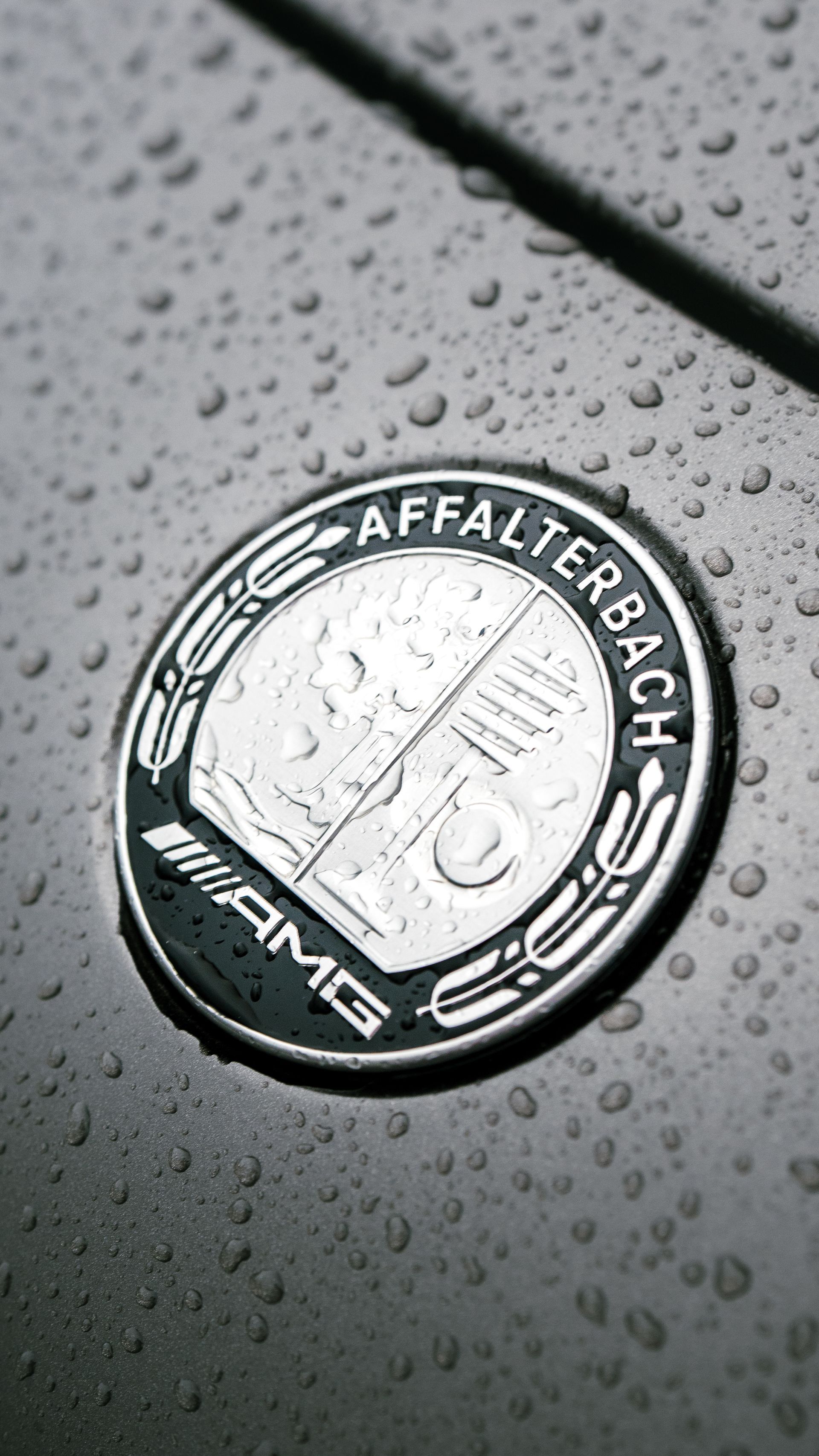 An AMG Affalterbach emblem on a wet, dark gray car surface.