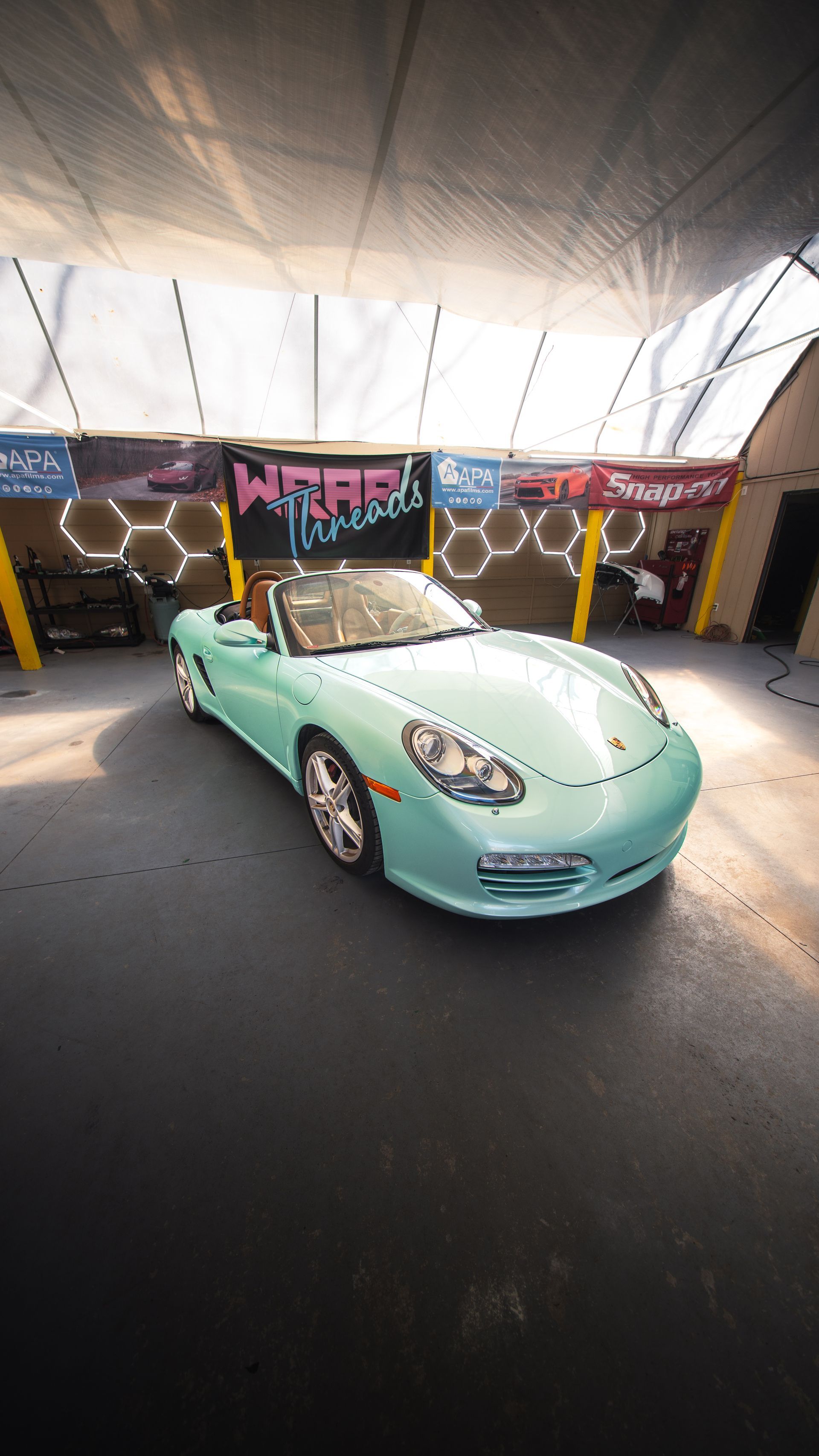 A mint green Porsche convertible parked in a garage with hexagon-patterned LED wall lights and a 