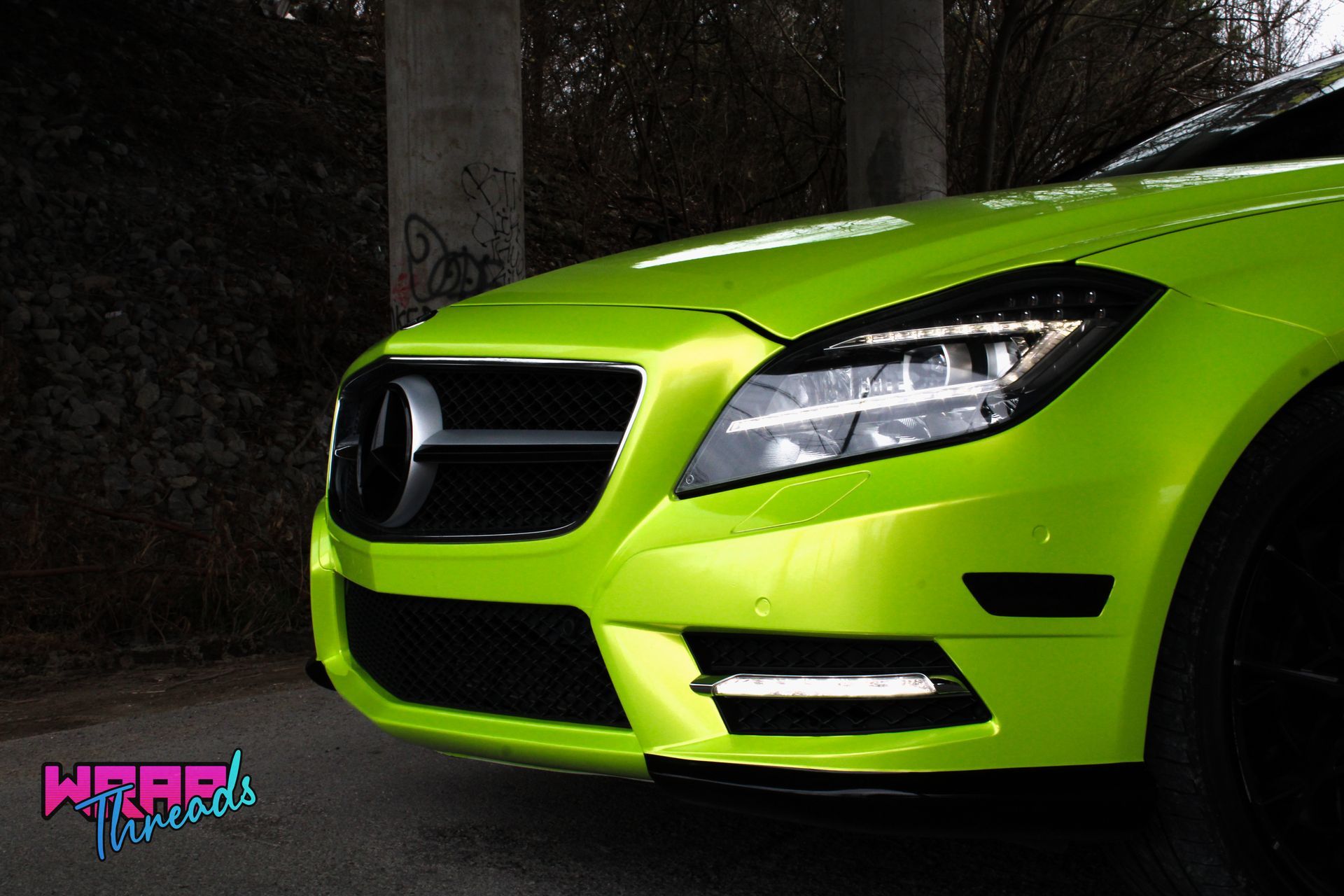 A lime green Mercedes-Benz sedan front end parked near a graffiti-covered concrete pillar.