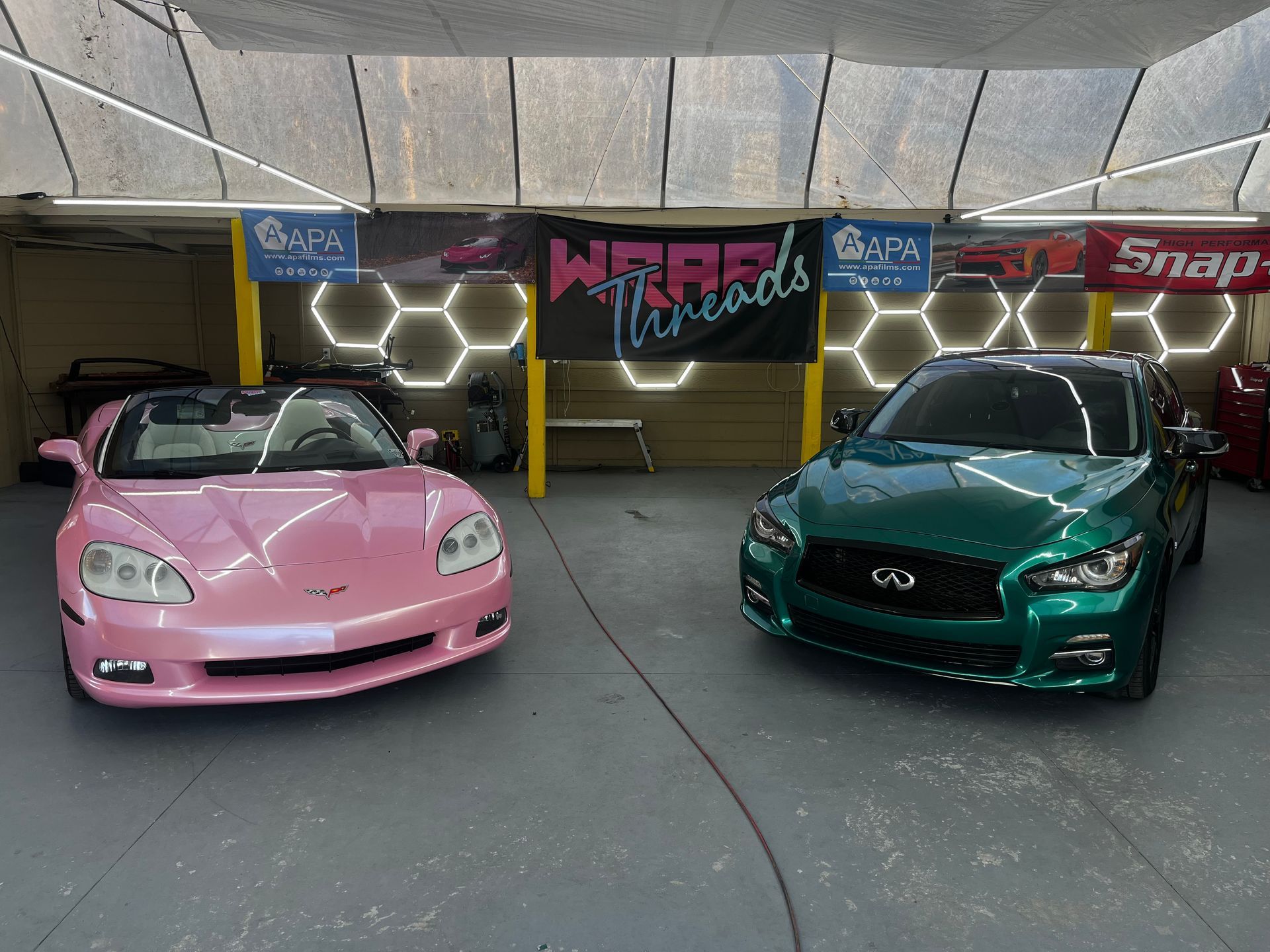 A pink convertible and a green sedan parked inside a garage with 