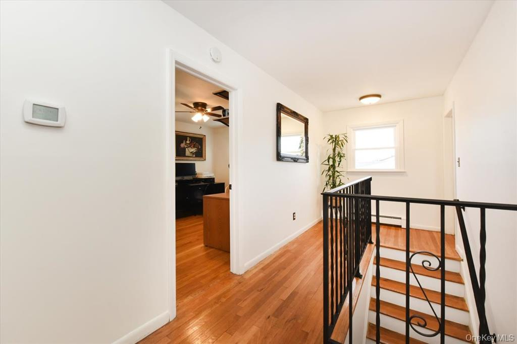 Hallway with hardwood floor, open doorway, staircase with black railing, white walls, and a window.