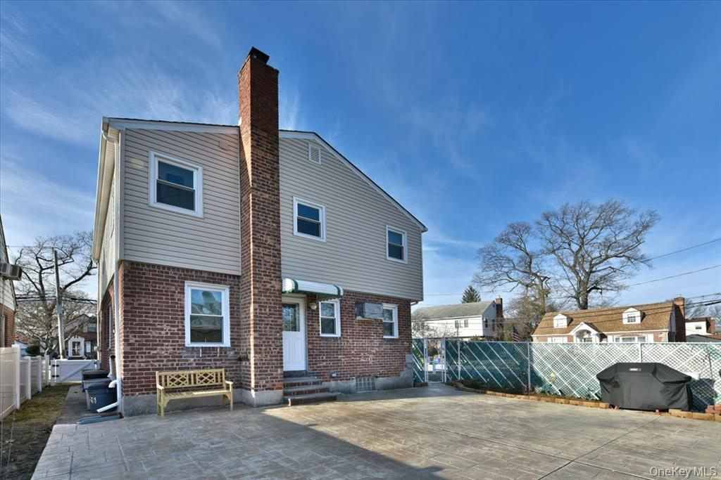Two story house with brick chimney and back entrance, adjacent concrete patio, sunny blue sky.