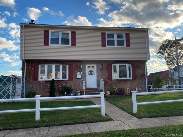 Two-story house with brick facade, beige siding, red shutters, and white picket fence.
