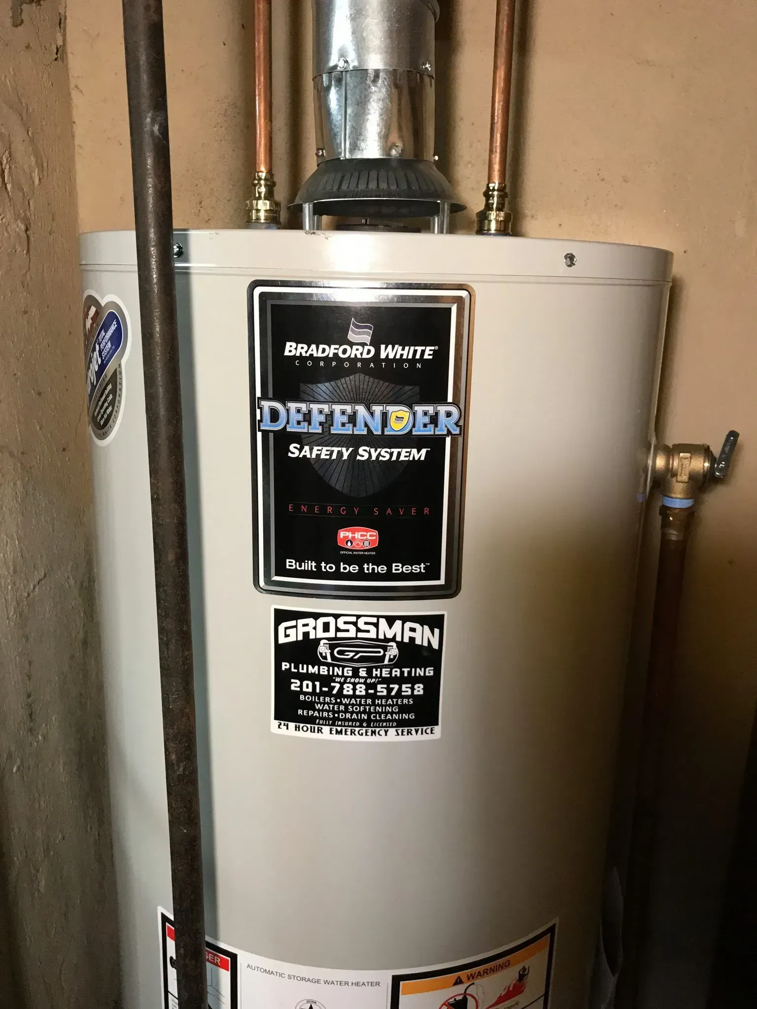 A white water heater is sitting in a room next to a pipe.