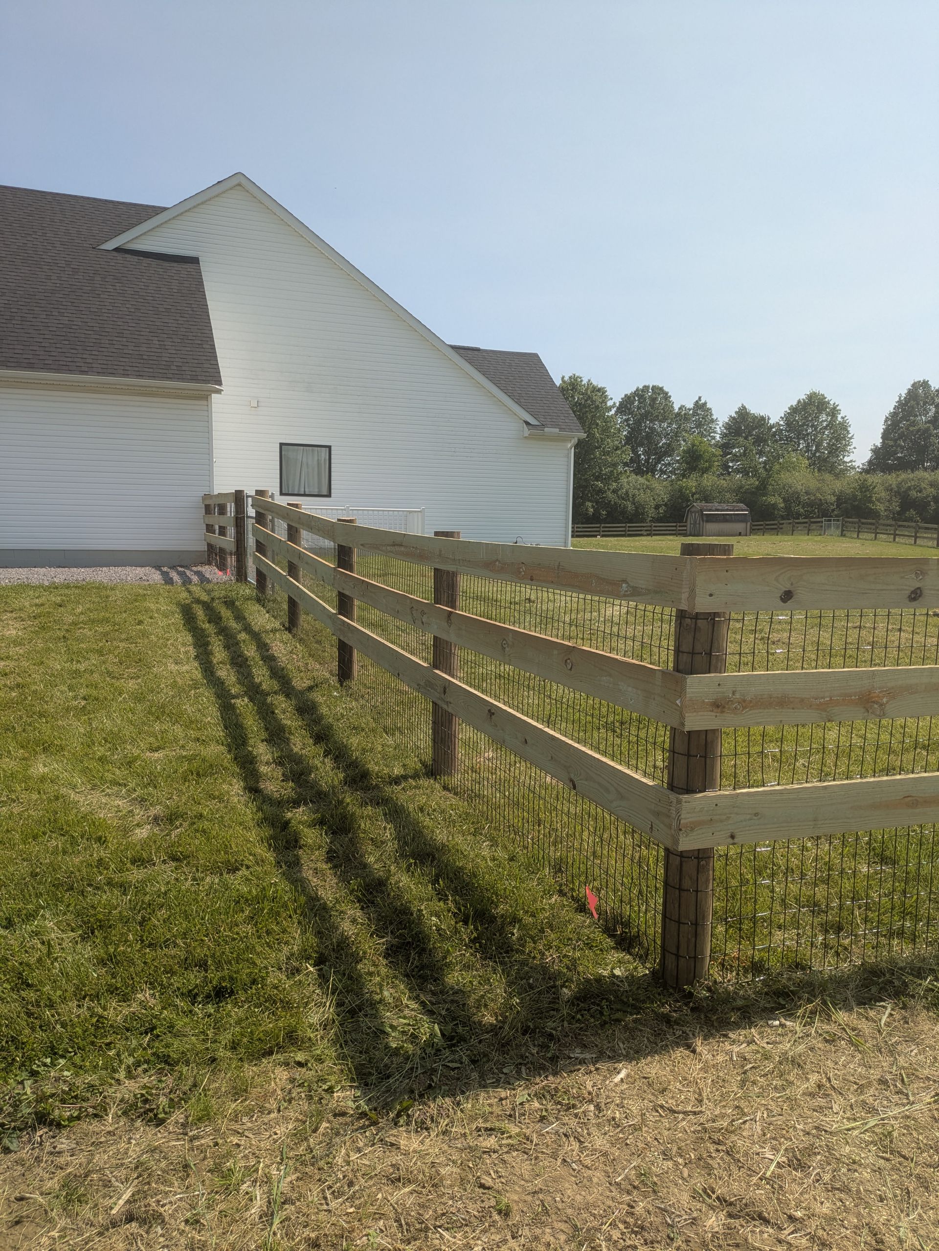 A wooden fence surrounds a grassy field in front of a white barn.