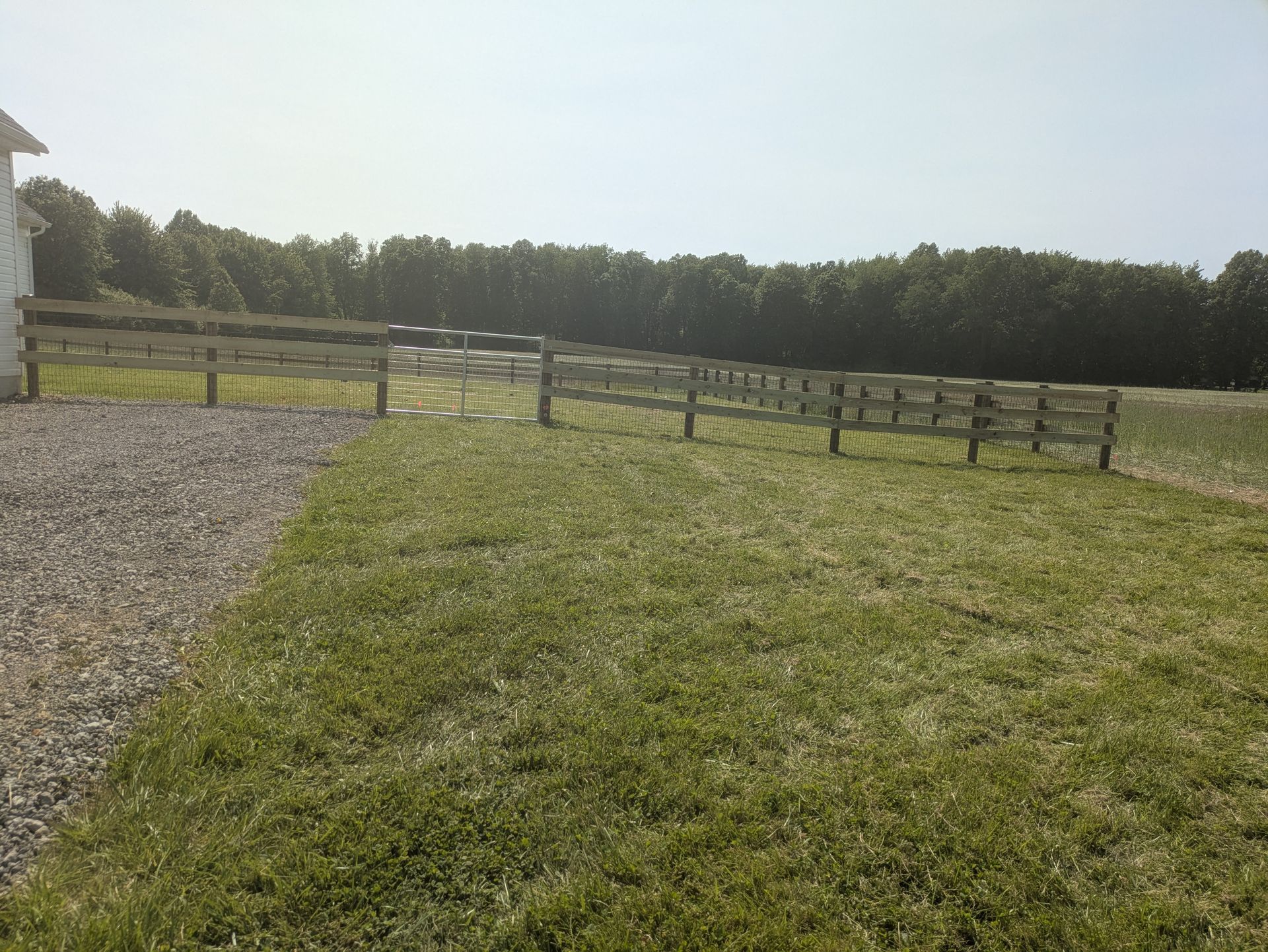 A wooden fence surrounds a grassy field with trees in the background