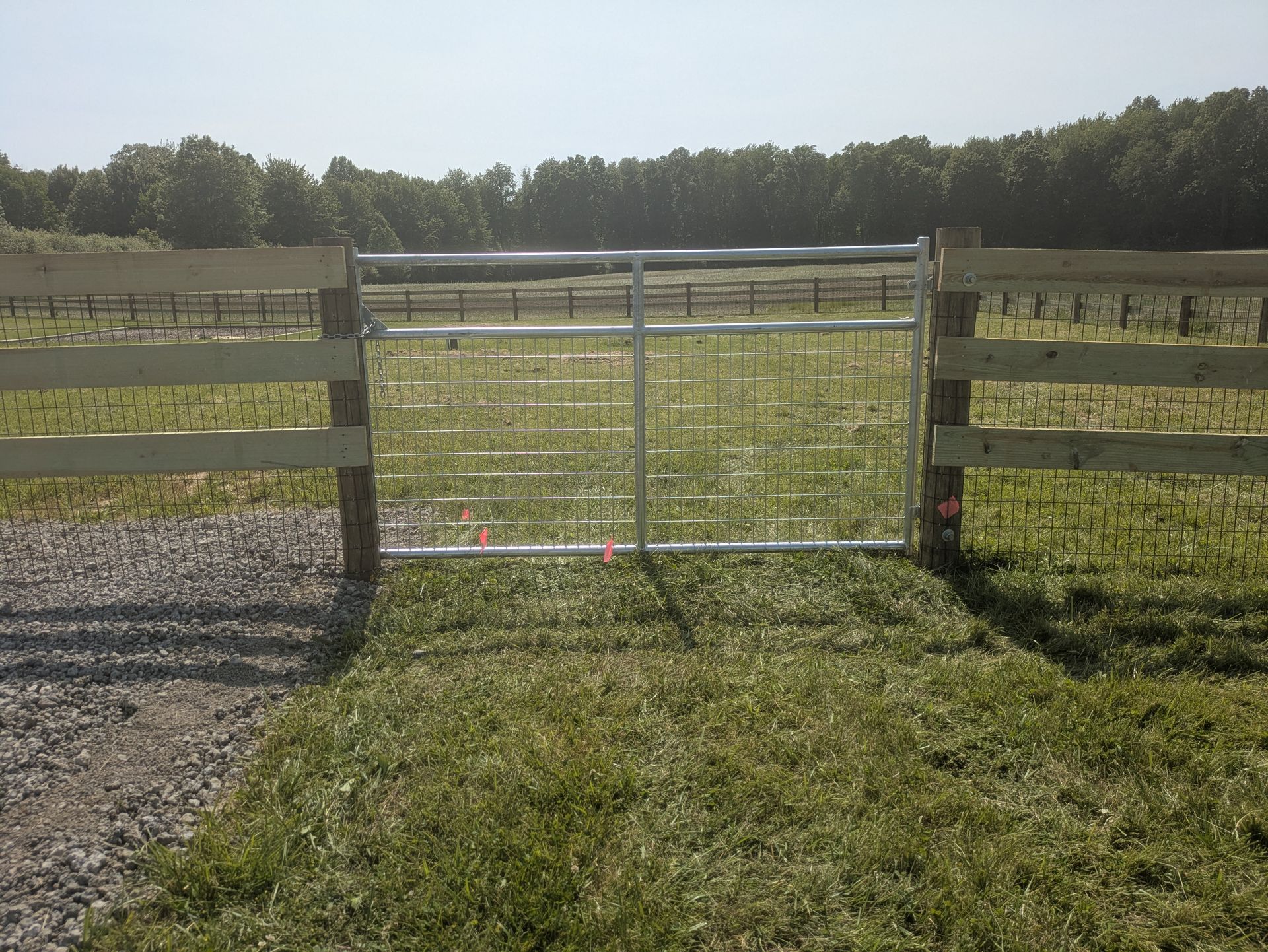 A wooden fence with a metal gate in the middle of a grassy field