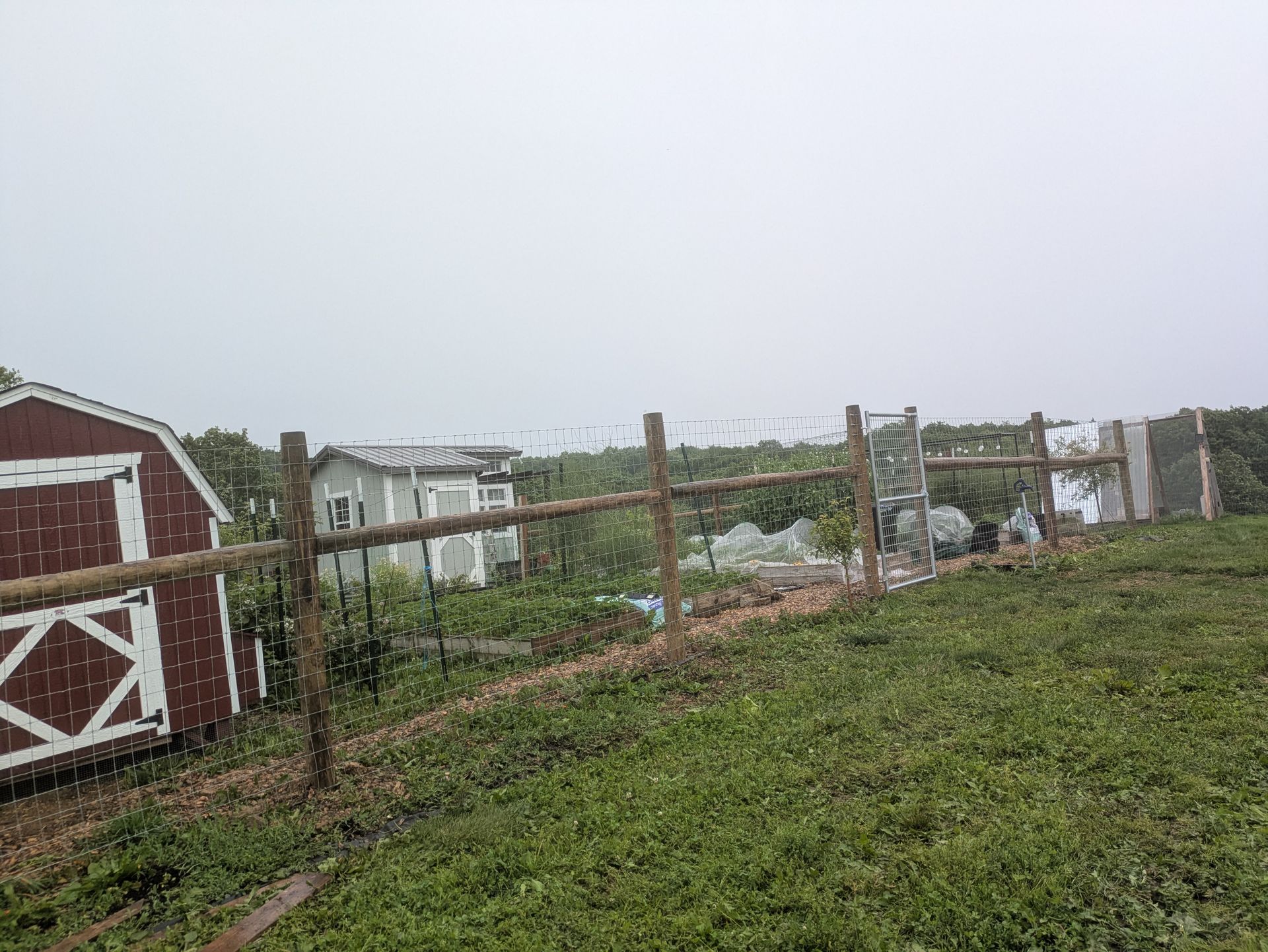 A wooden fence surrounds a field with a red barn in the background.