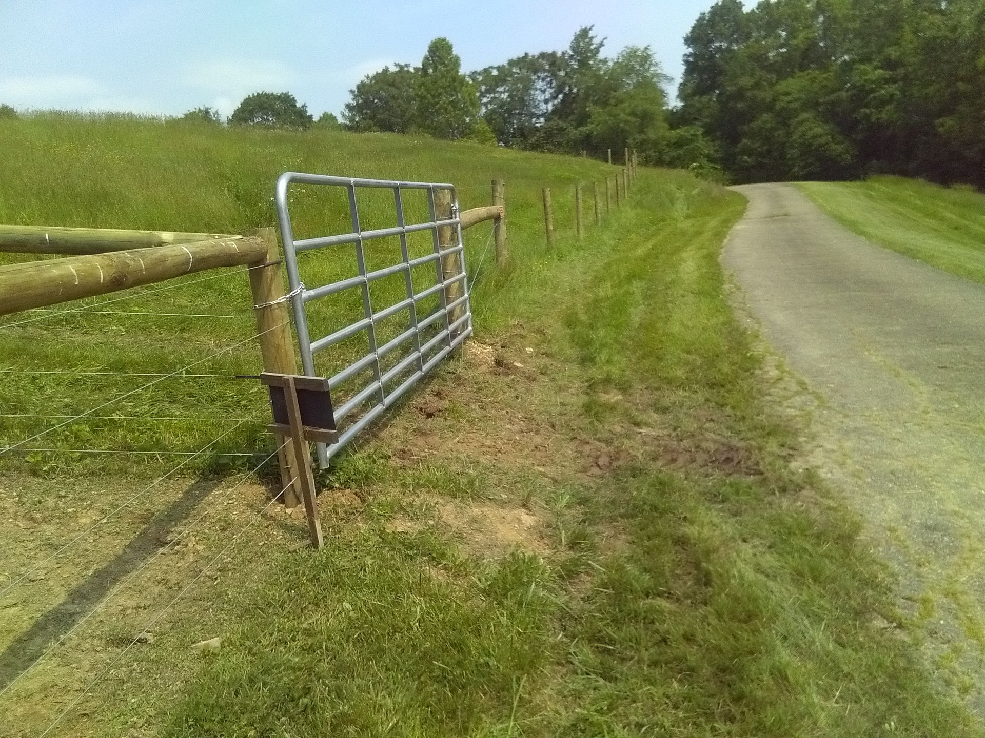 A metal gate is sitting on the side of a dirt road
