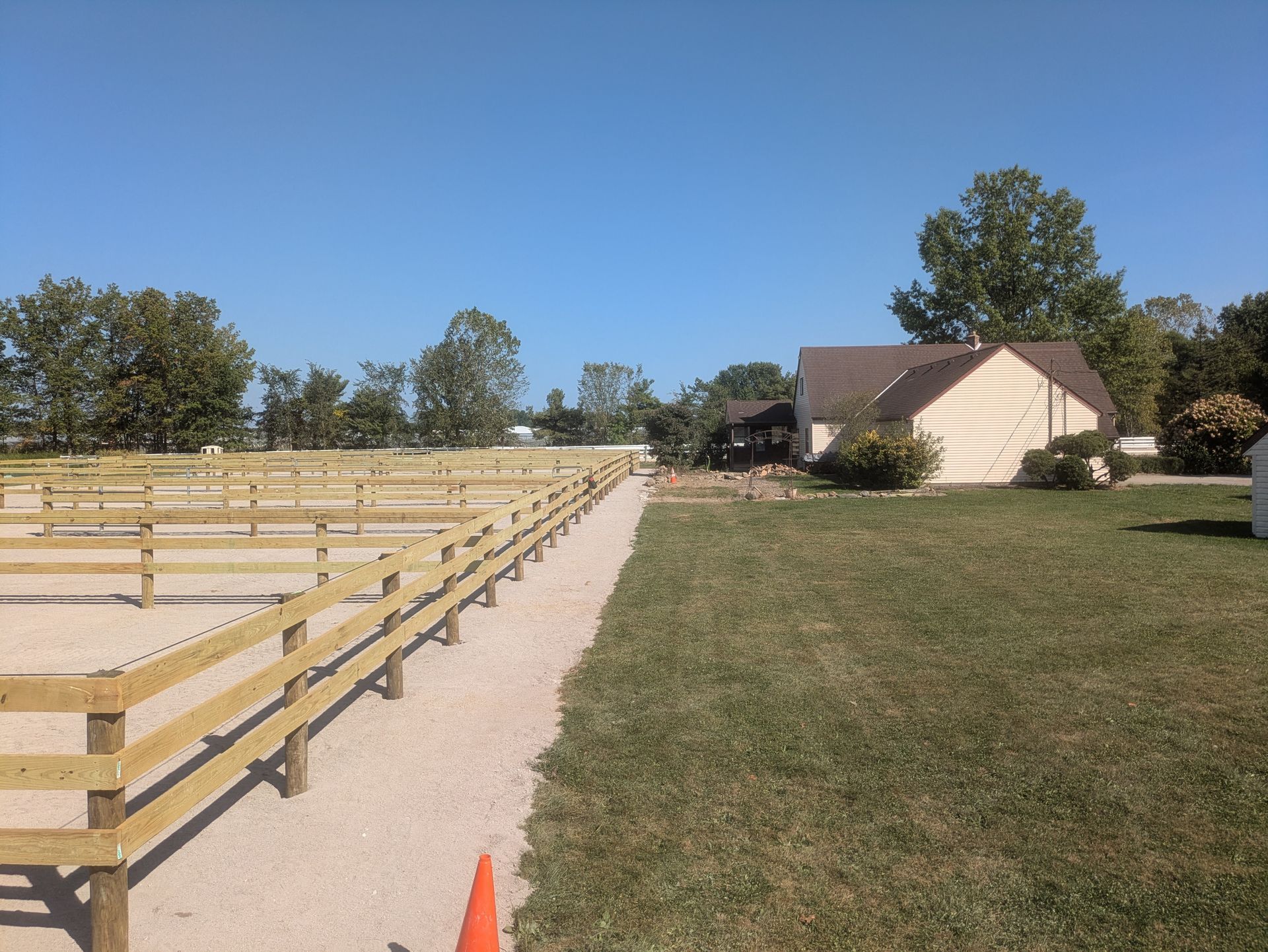 Wooden fence bordering gravel path next to grassy area, house and clear blue sky in the background.
