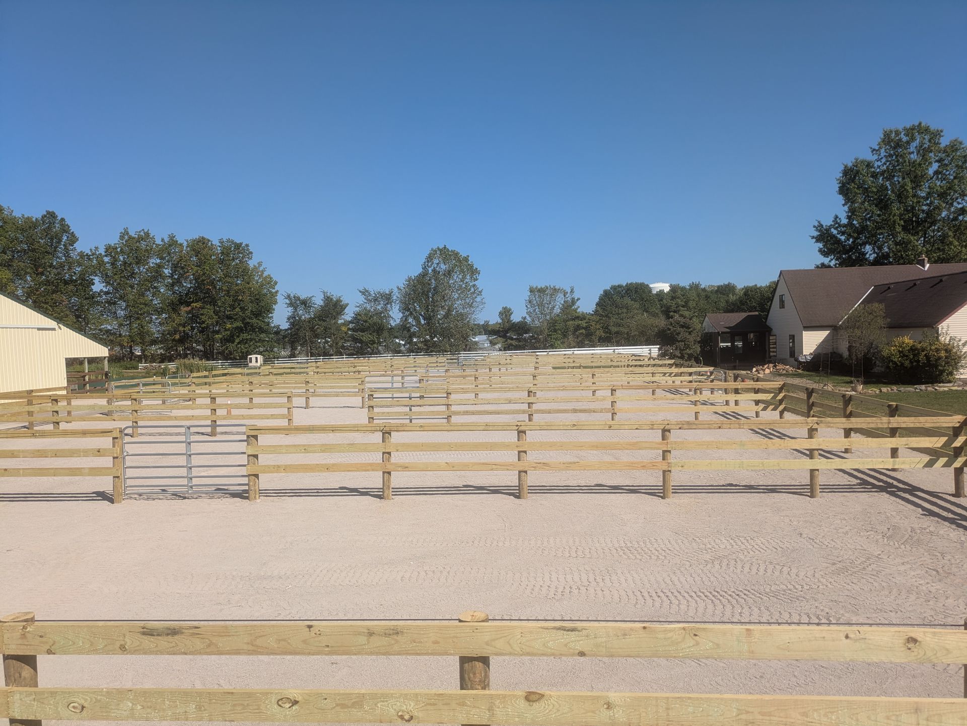 Horse riding arena with wooden fences, light-colored sand, and a blue sky.