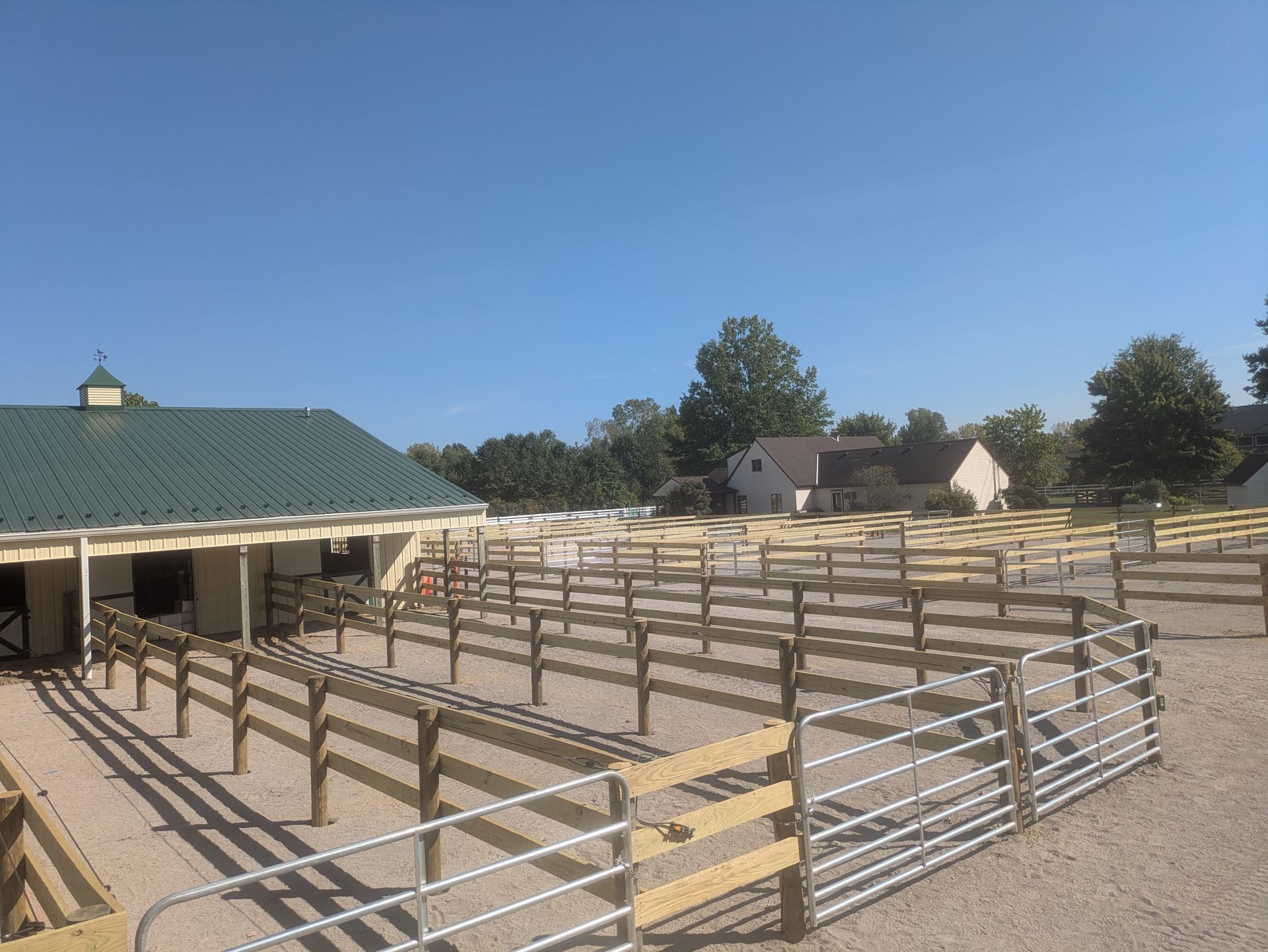 Horse stables with many fenced paddocks on a gravel base under a blue sky.