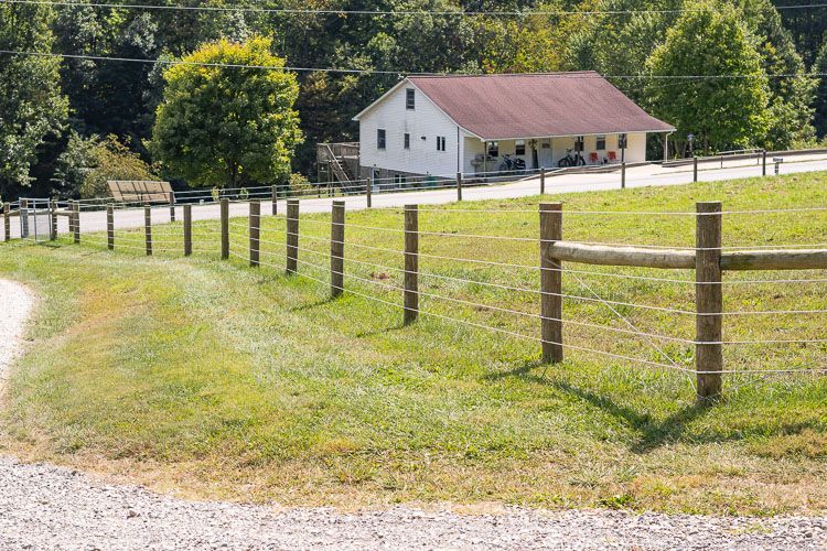 A fence surrounds a grassy field with a house in the background.