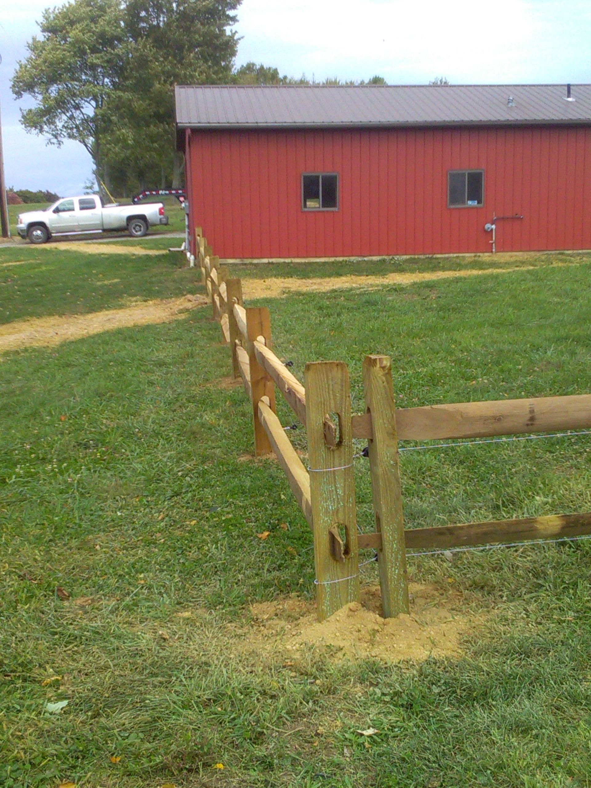 A wooden fence surrounds a grassy field in front of a red barn.