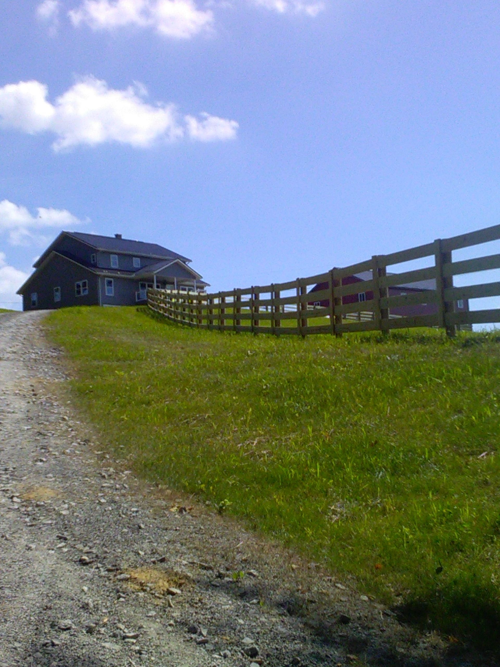 A dirt road leading to a house with a wooden fence