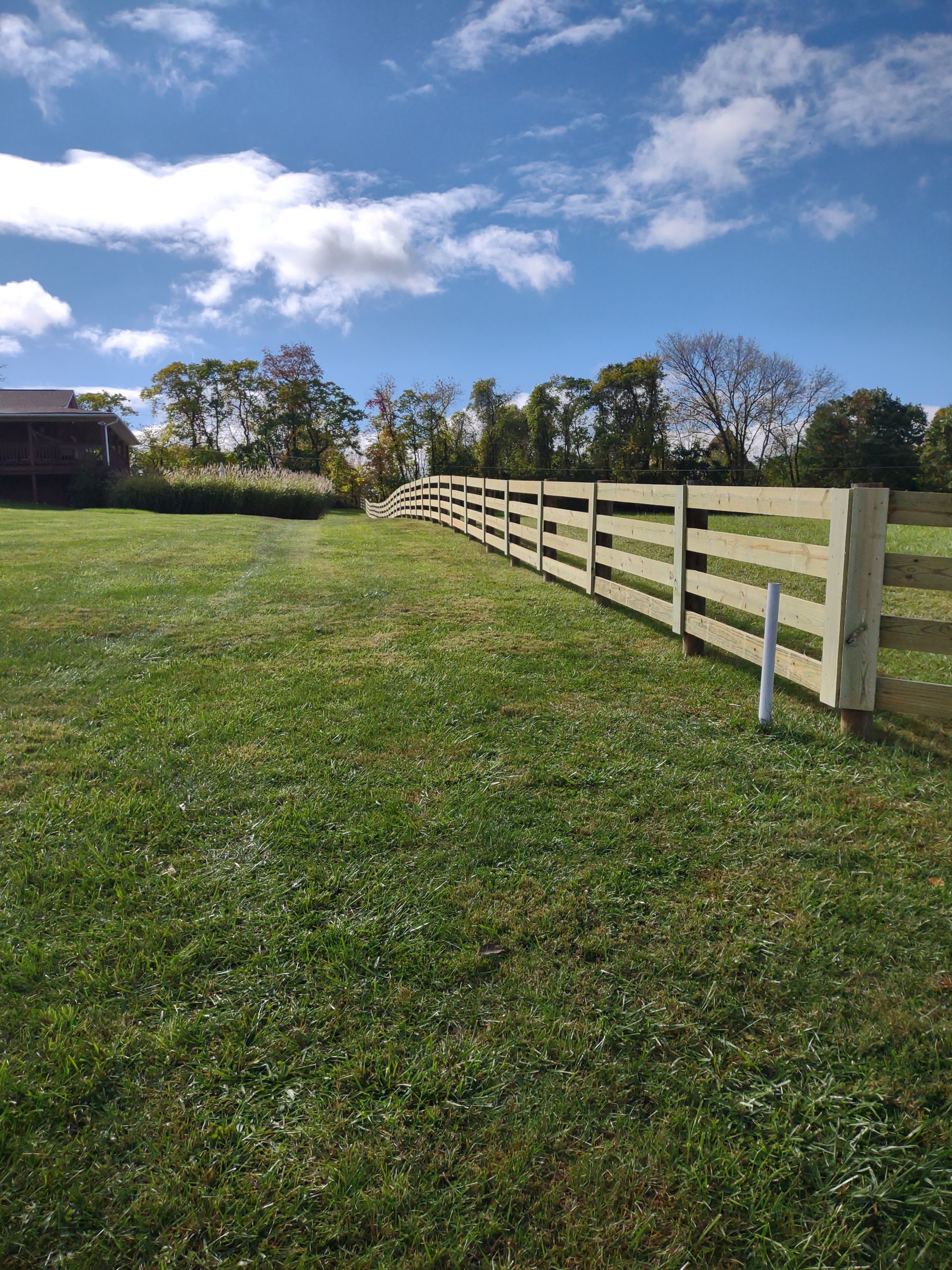 A wooden fence surrounds a grassy field with a barn in the background.