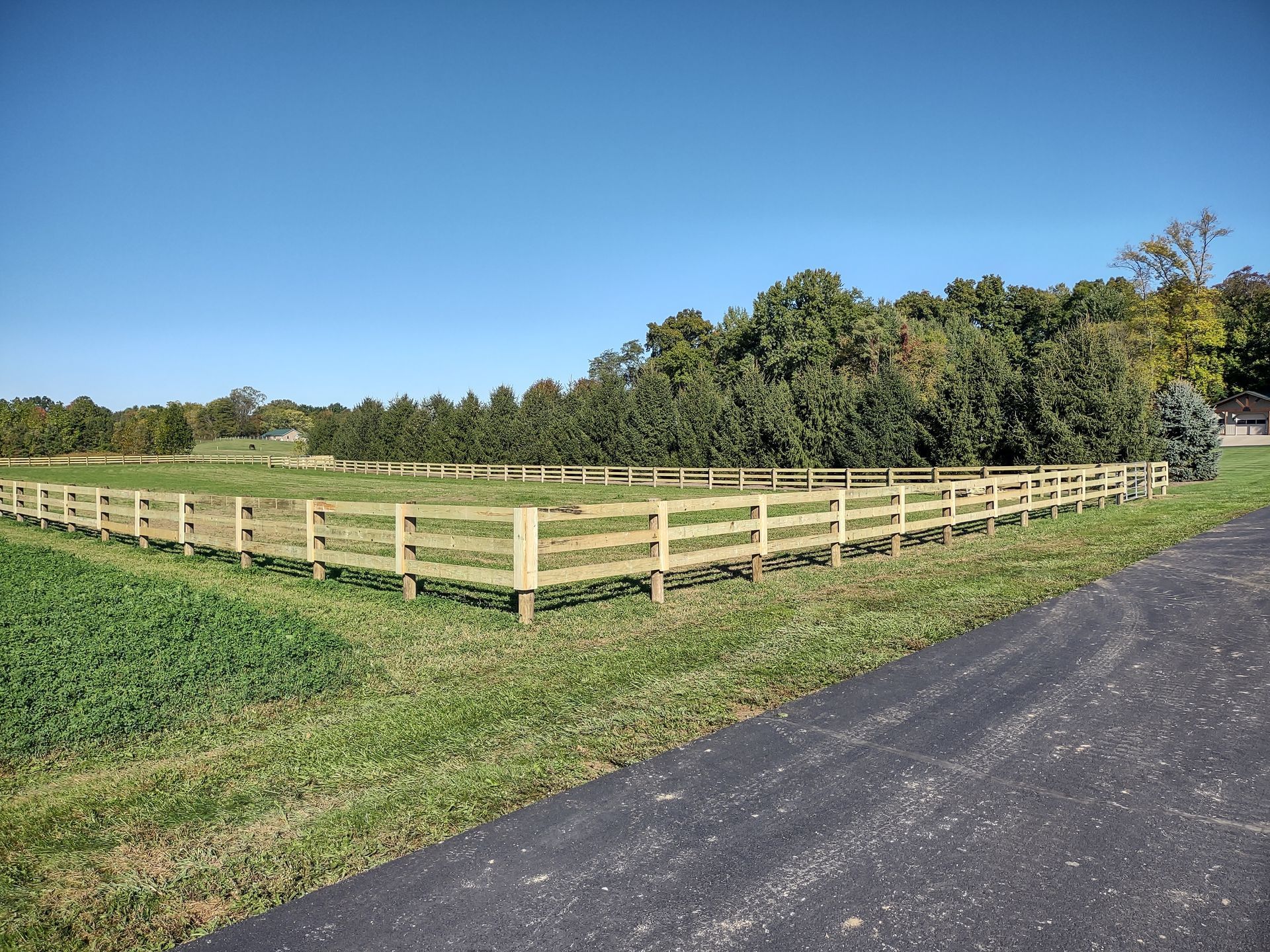 A wooden fence surrounds a grassy field next to a road.