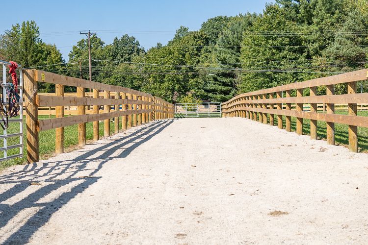 A wooden fence surrounds a dirt road in a field.