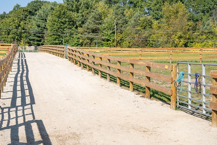 A wooden fence surrounds a dirt road in a field.