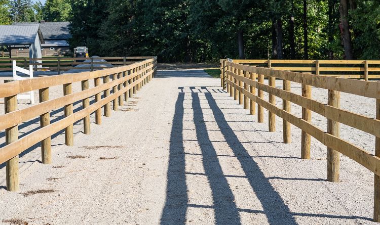A wooden fence along a dirt road with trees in the background.