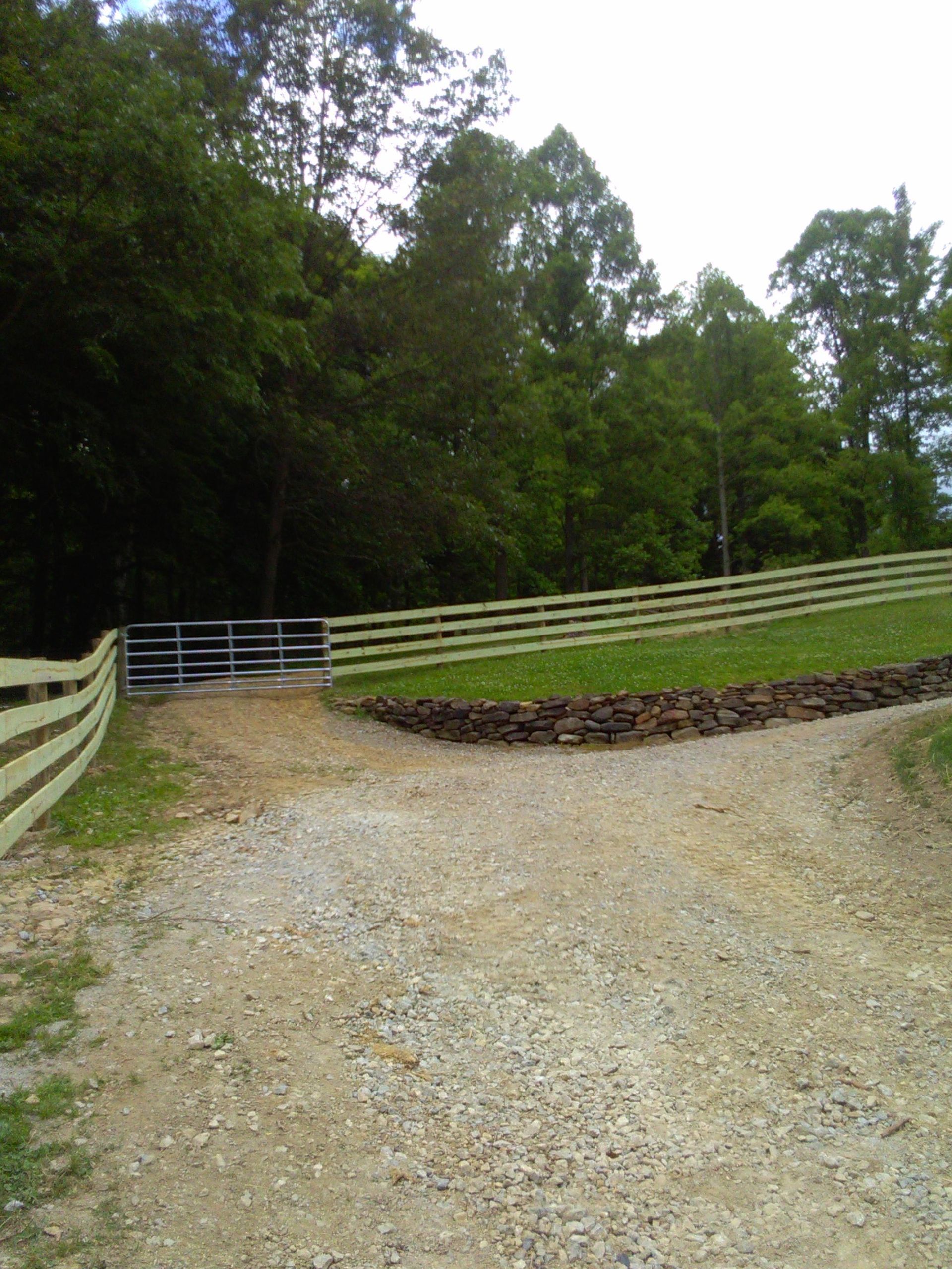 A dirt road with a wooden fence and a gate in the background.
