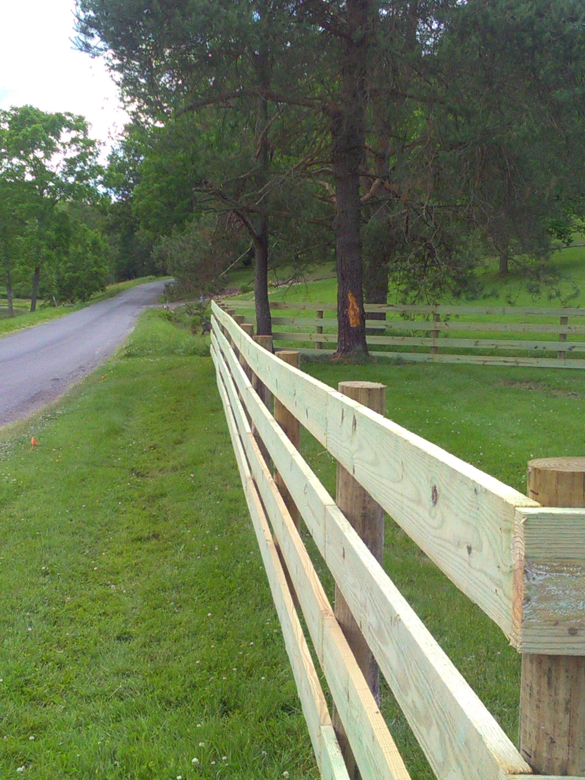A wooden fence surrounds a grassy field next to a road.