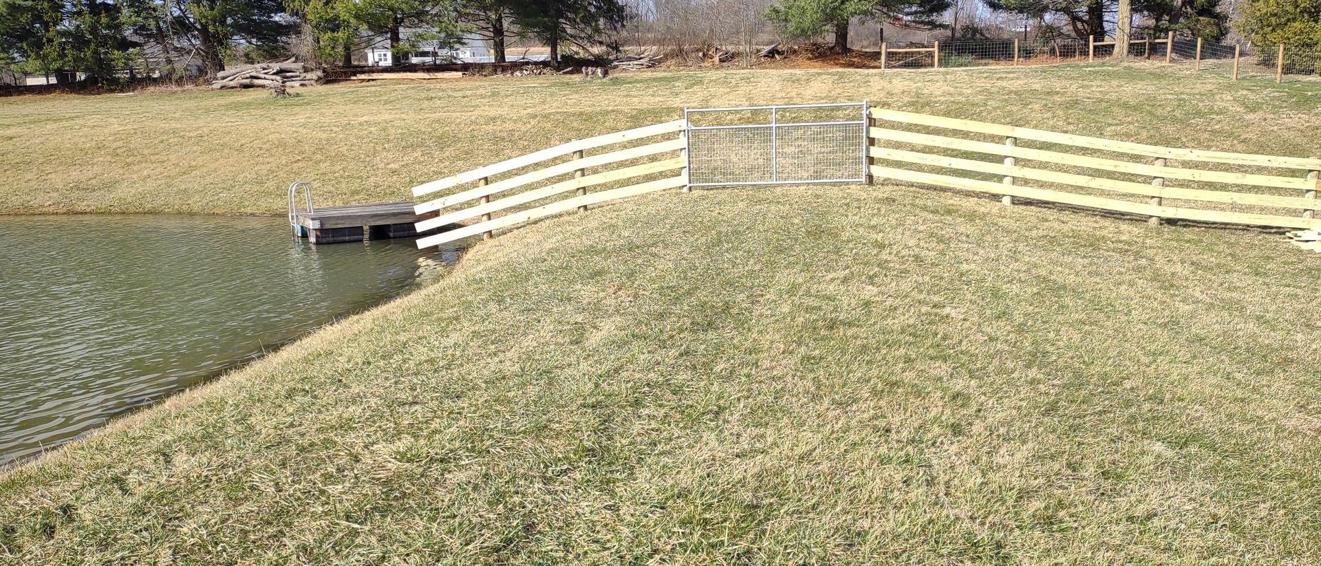 A wooden fence surrounds a pond in a grassy field.
