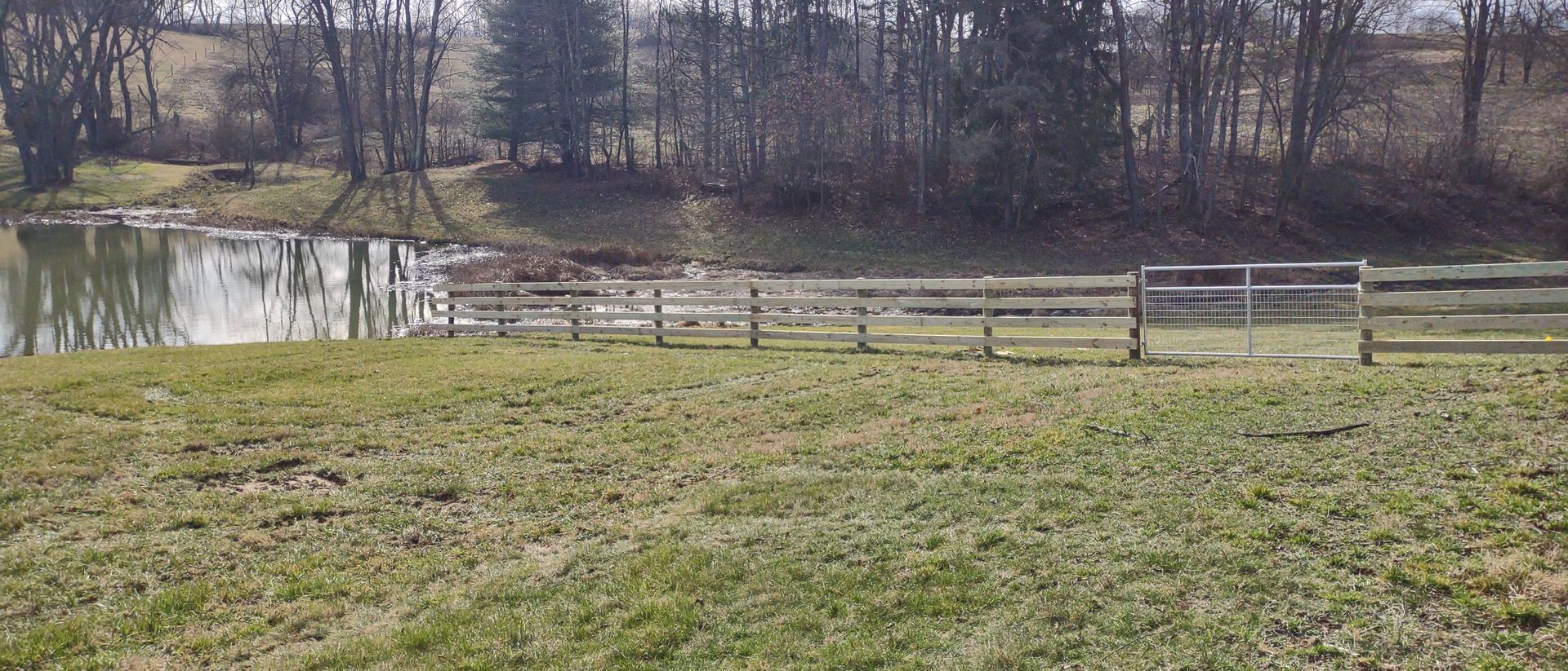 A grassy field with a fence and a pond in the background.