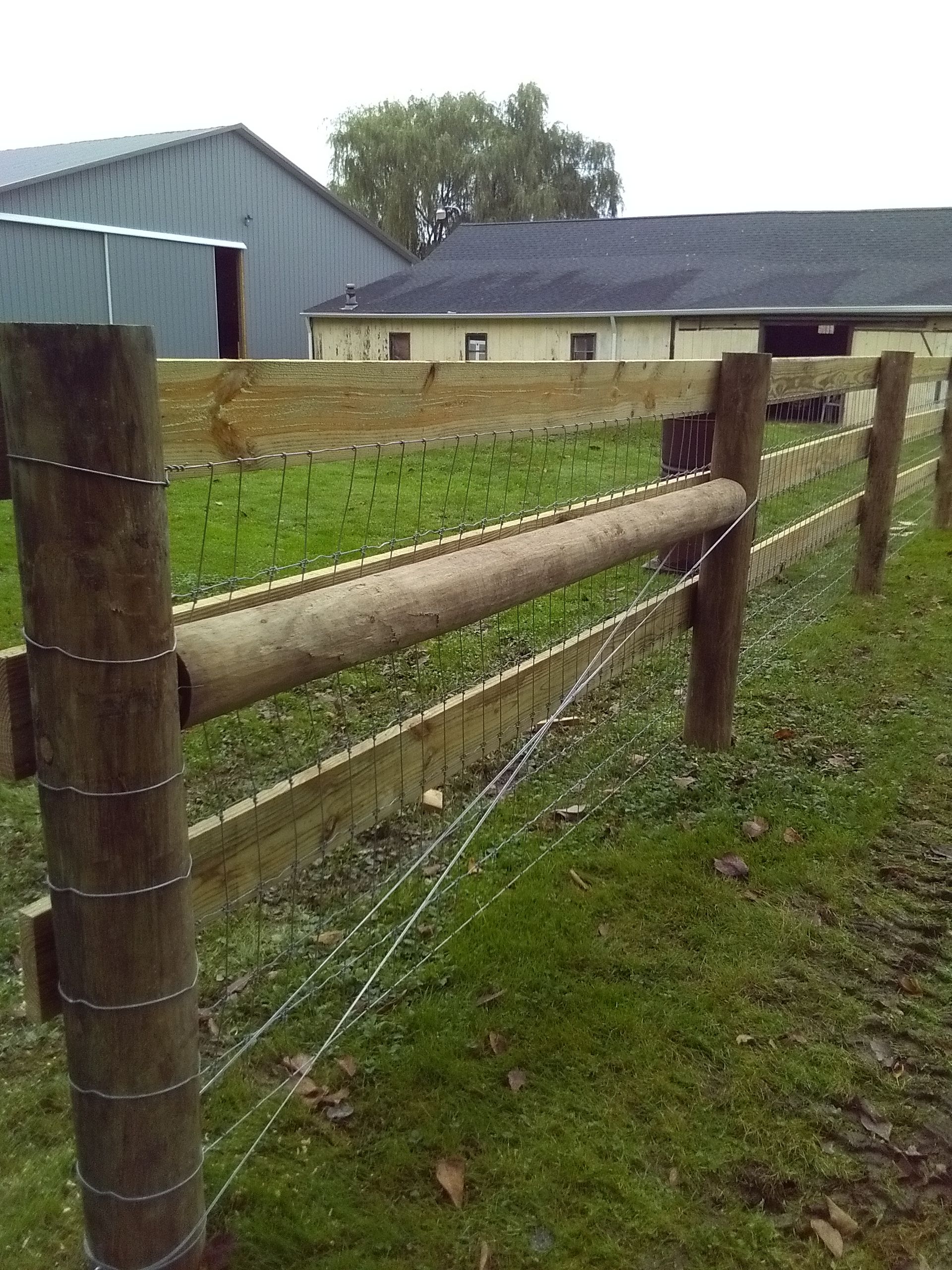 A wooden fence surrounds a grassy field with a building in the background