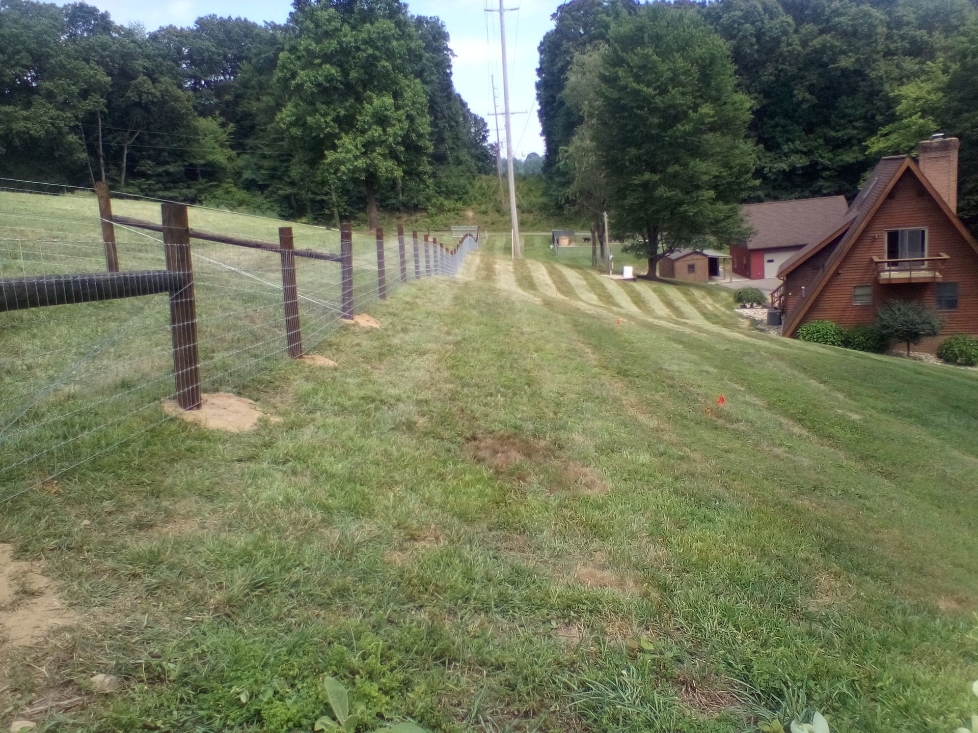 A rural scene with a fence, grassy area, trees, and a house on a small hill.
