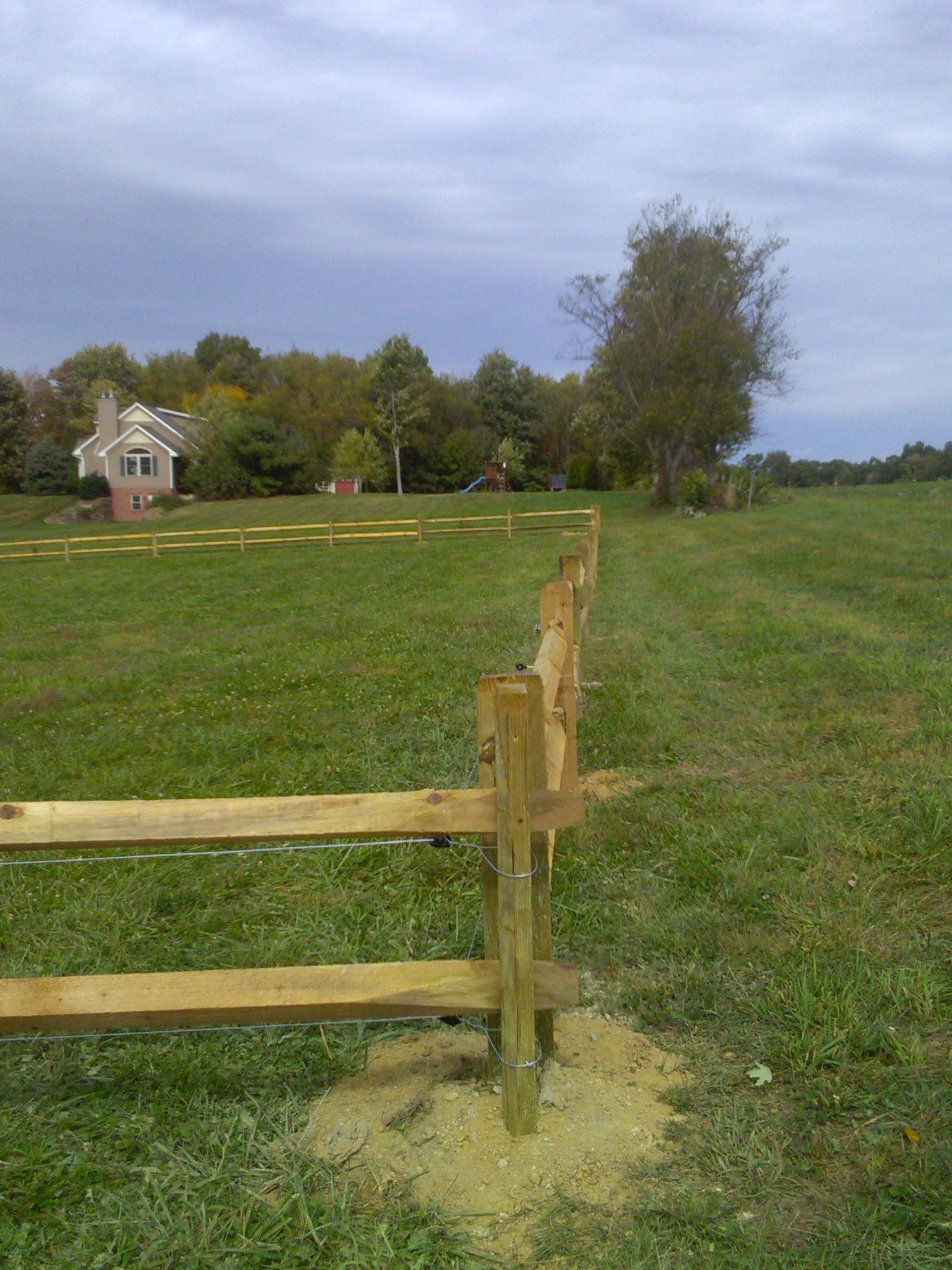 A wooden fence surrounds a grassy field with a house in the background.