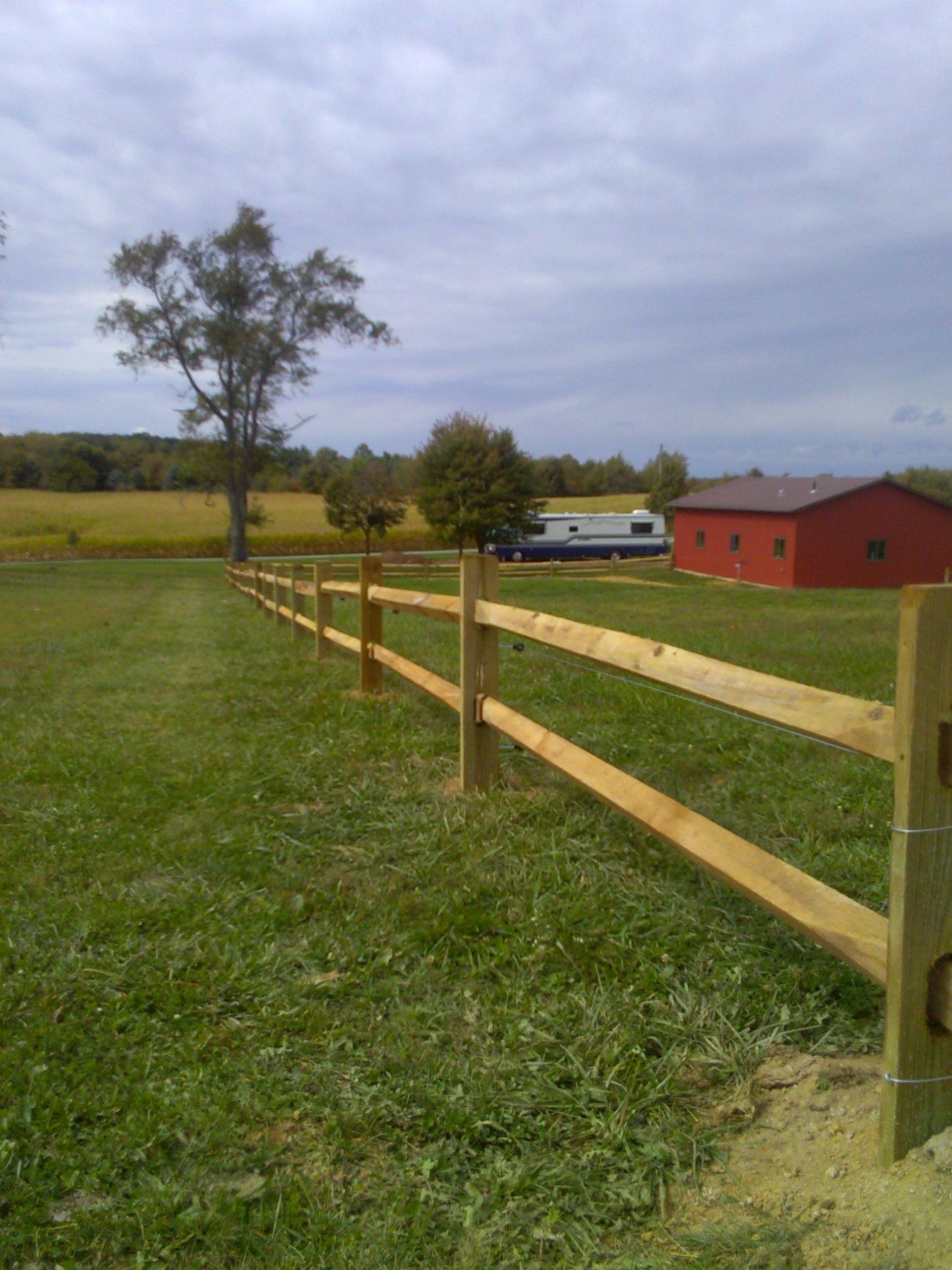 A wooden fence surrounds a grassy field with a red barn in the background.