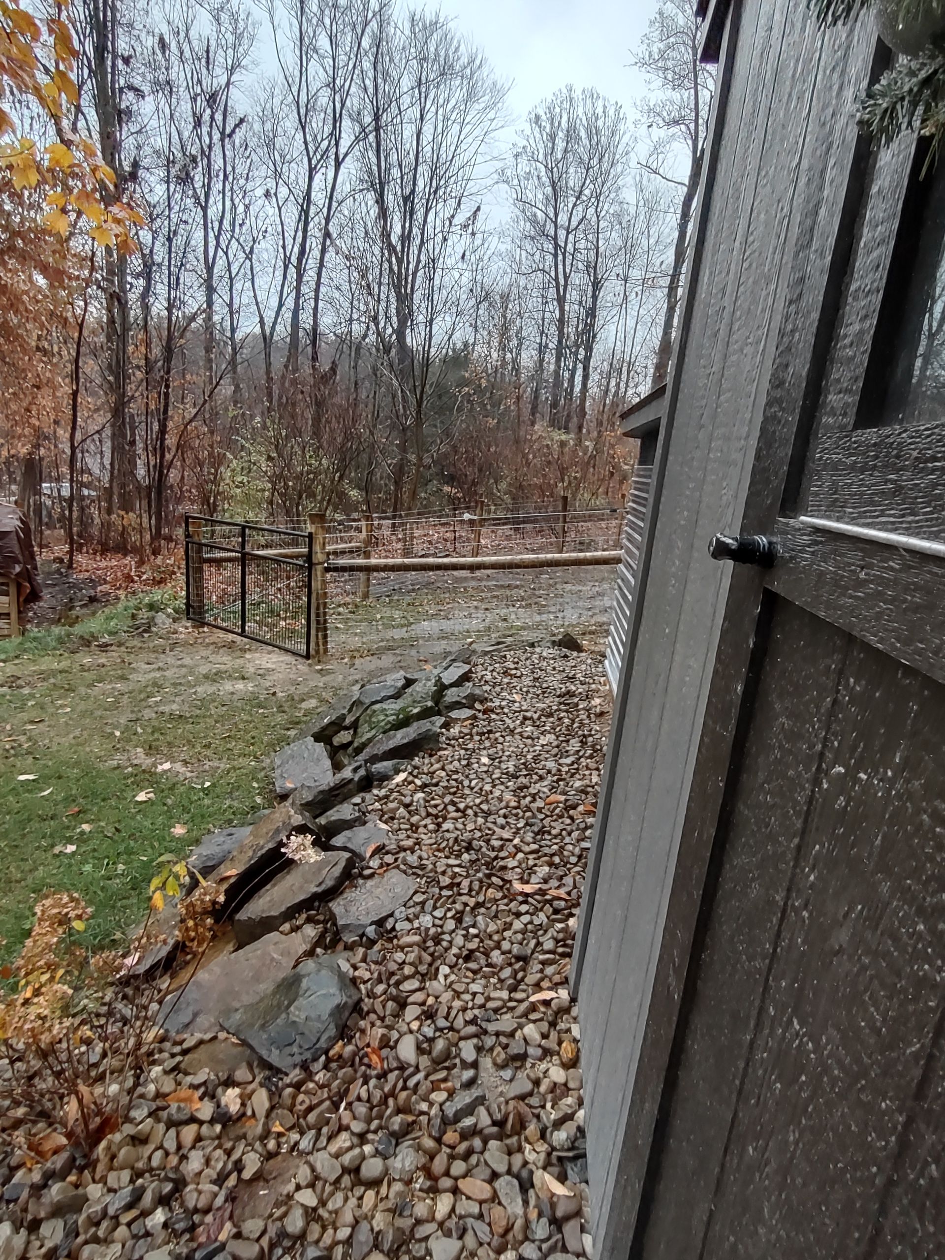 A wooden fence with a stone wall and trees in the background.