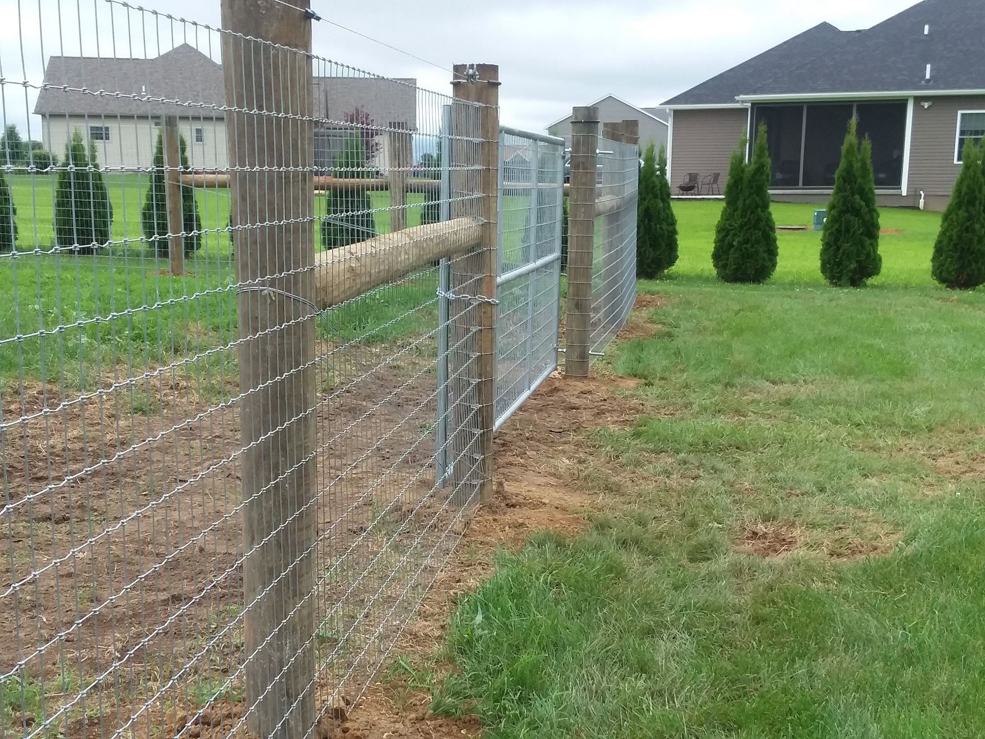 A barbed wire fence surrounds a yard with a house in the background