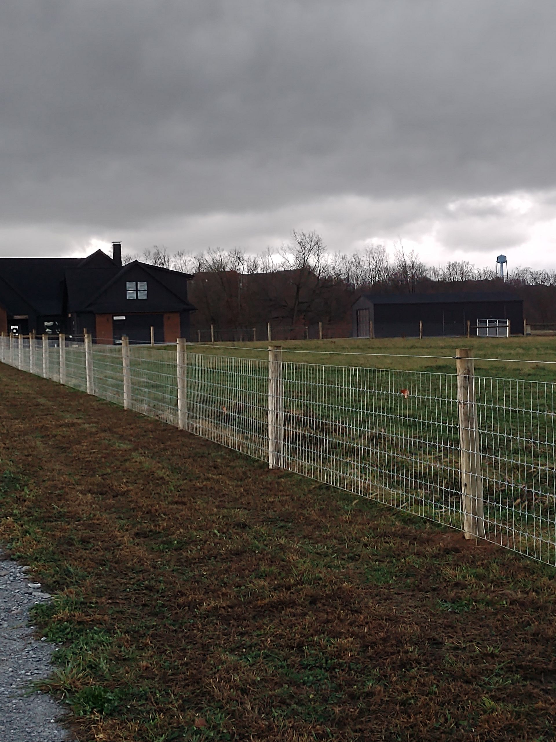 A fence along the side of a road with a house in the background