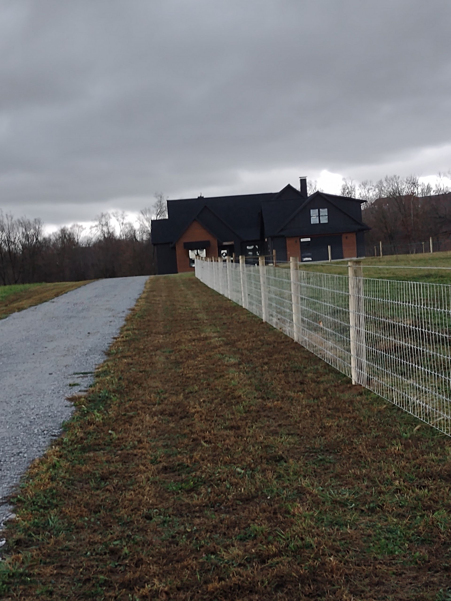 A white fence along a dirt road with a house in the background
