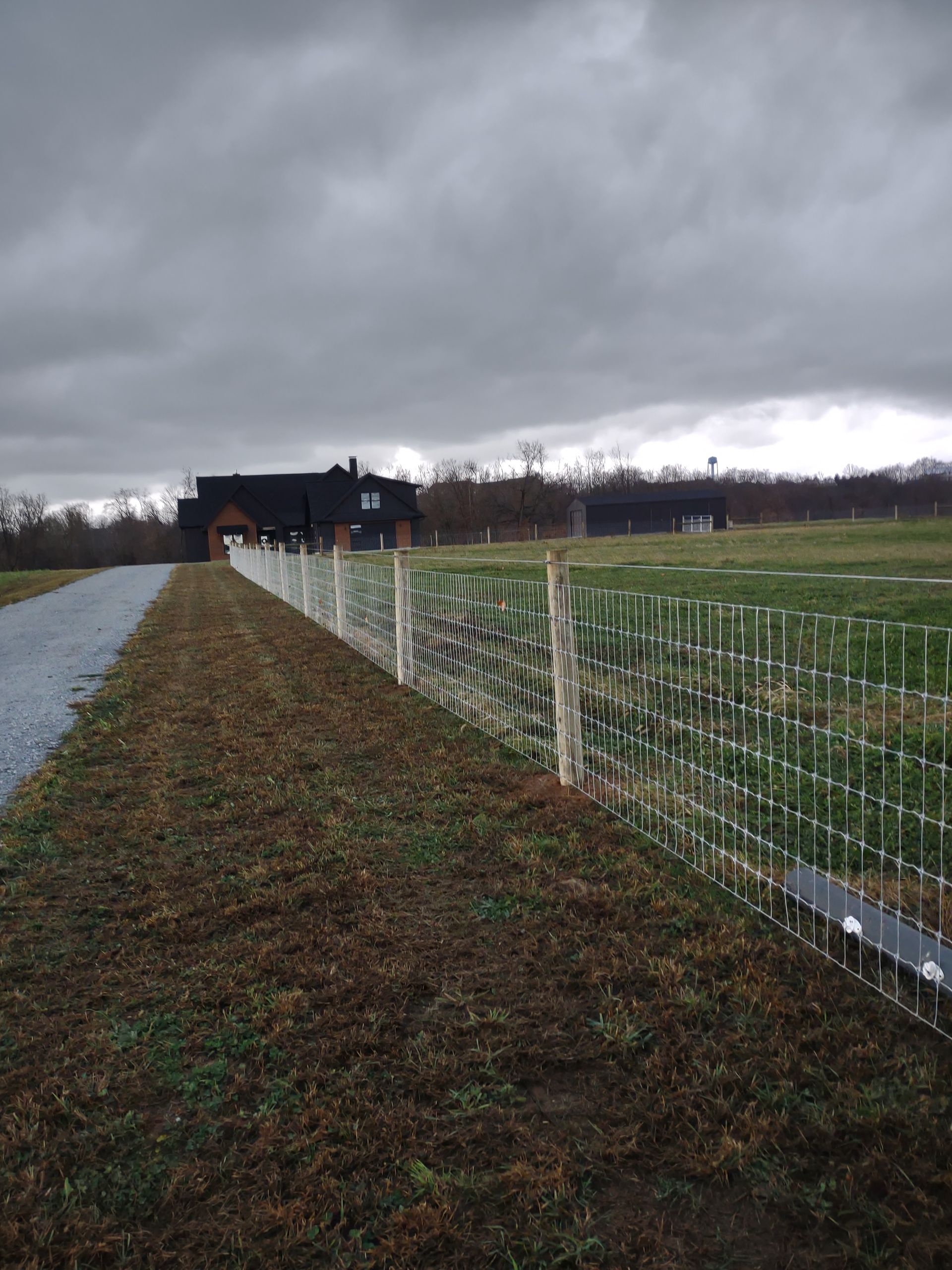 A fence surrounds a field with a house in the background on a cloudy day