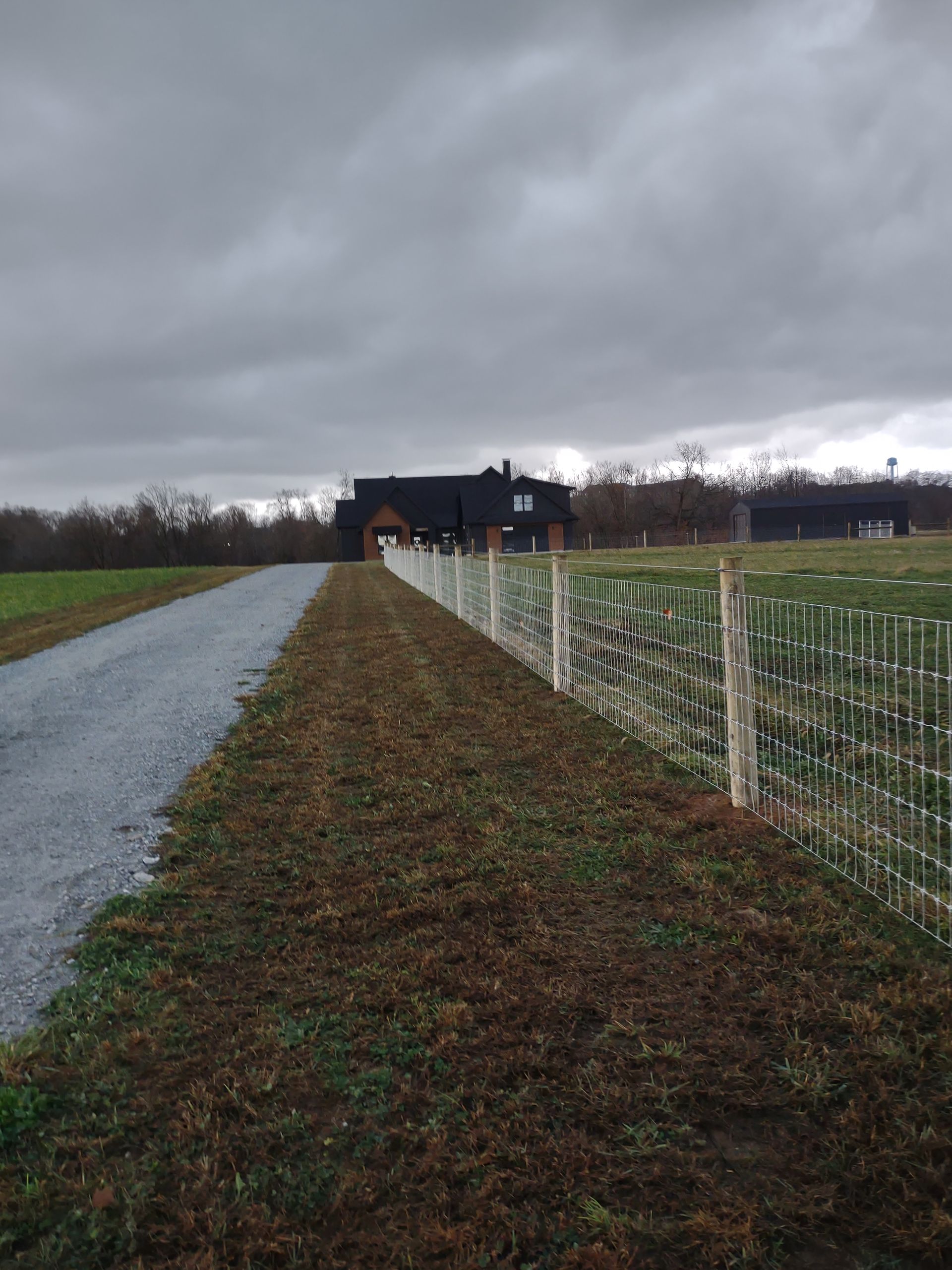 A fence along the side of a road with a house in the background