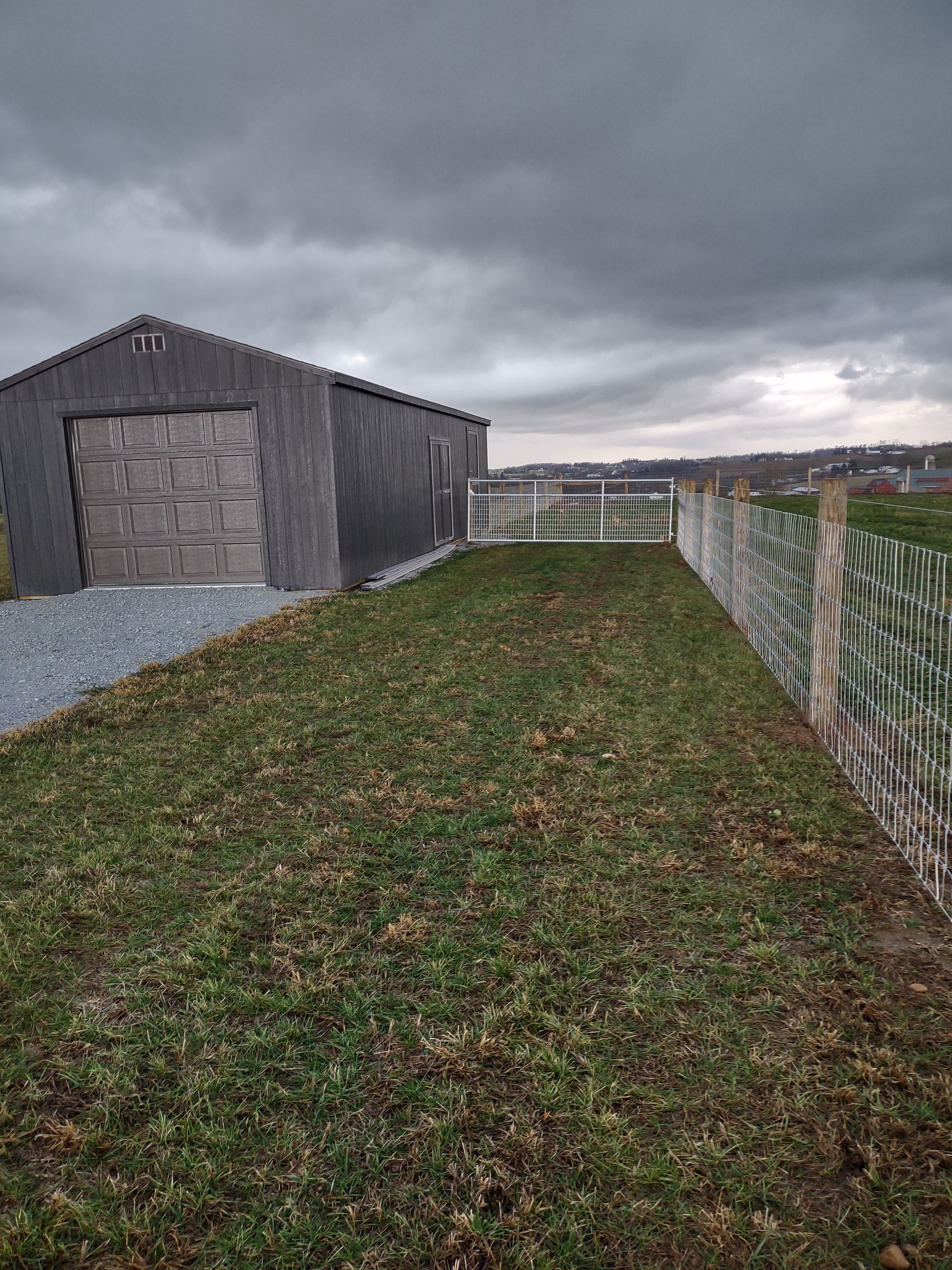 A shed is sitting in the middle of a grassy field next to a fence
