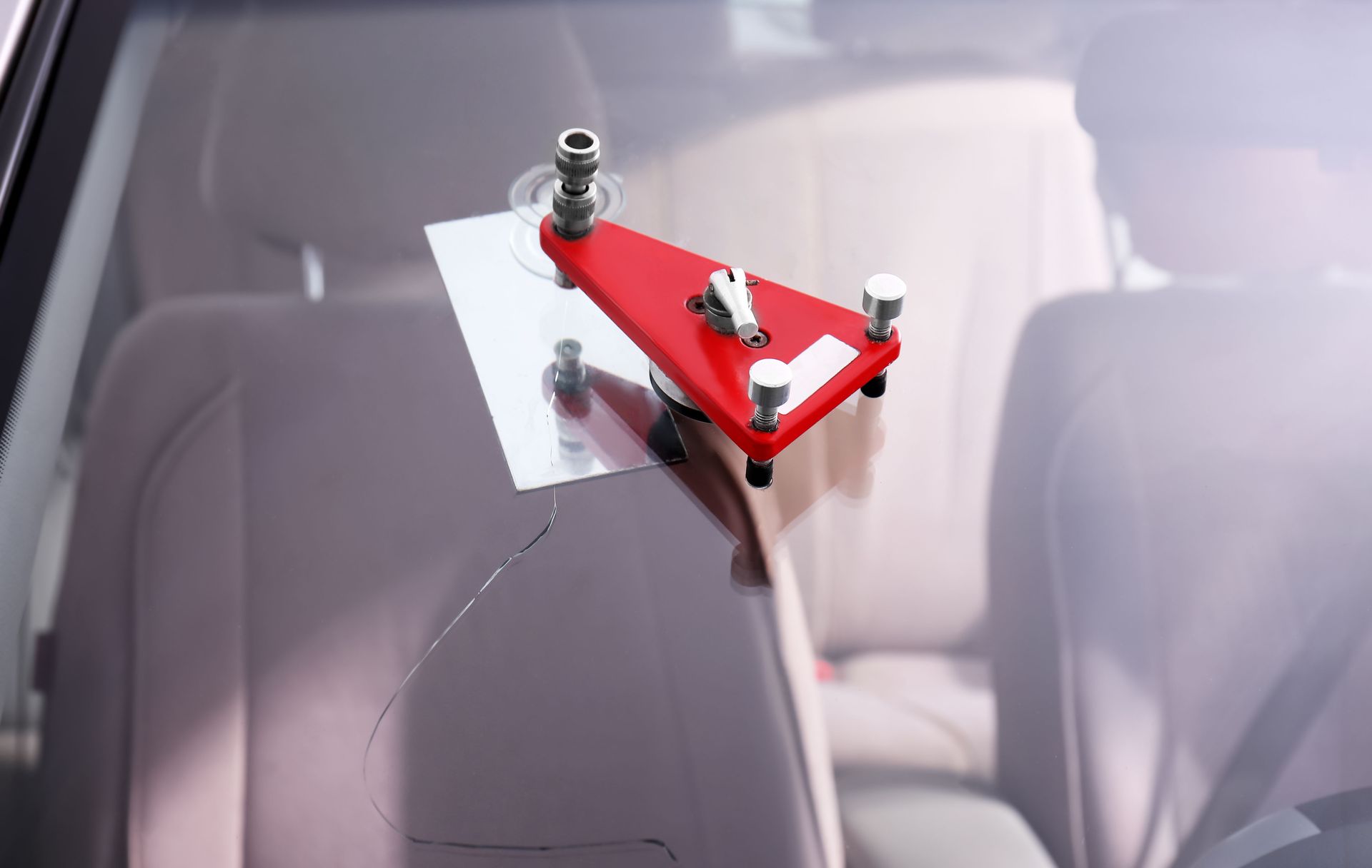Red windshield repair tool clamped to a car windshield over a crack.