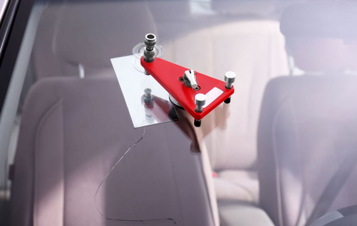 Red windshield repair tool clamped to a car windshield over a crack.