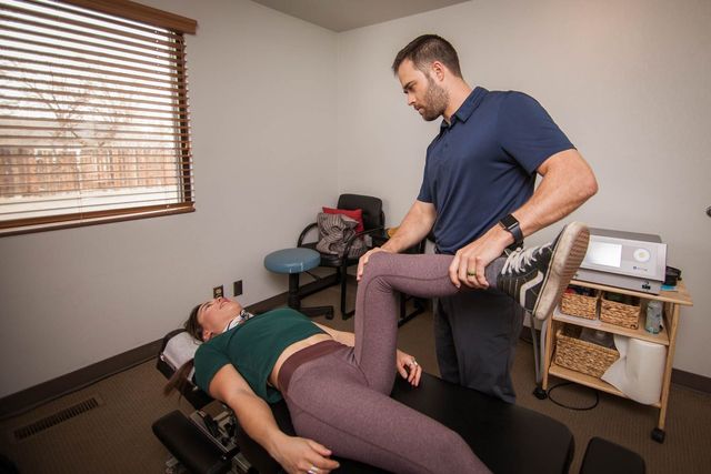 Physical therapist adjusting a patient's leg on a treatment table in a clinic room