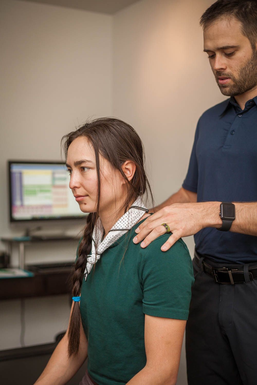 Man standing behind seated woman, placing hands on her shoulders in a clinical setting