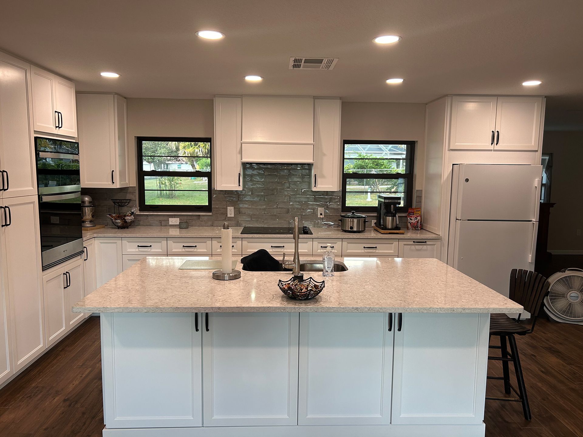 A kitchen with white cabinets, granite counter tops, and a large island