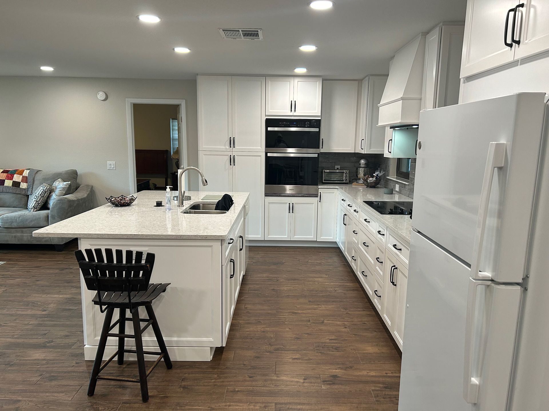 A kitchen with white cabinets, stainless steel appliances, a large island, and a refrigerator