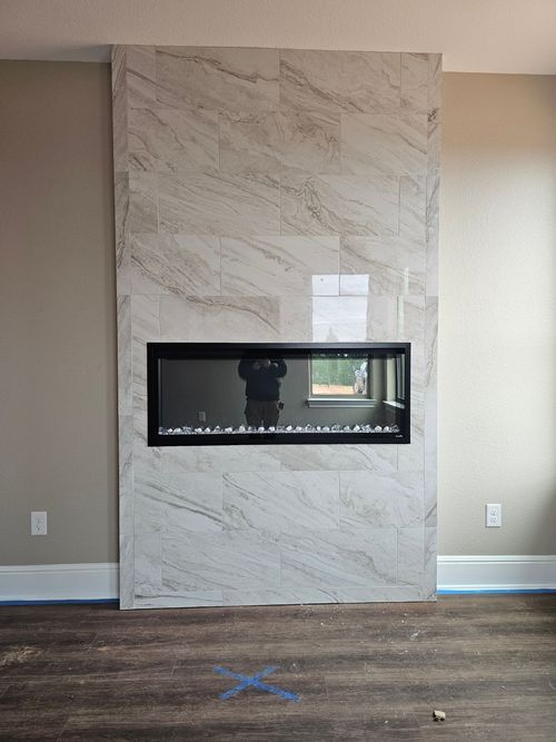 Fireplace with rectangular black firebox set in a marble-tiled wall.